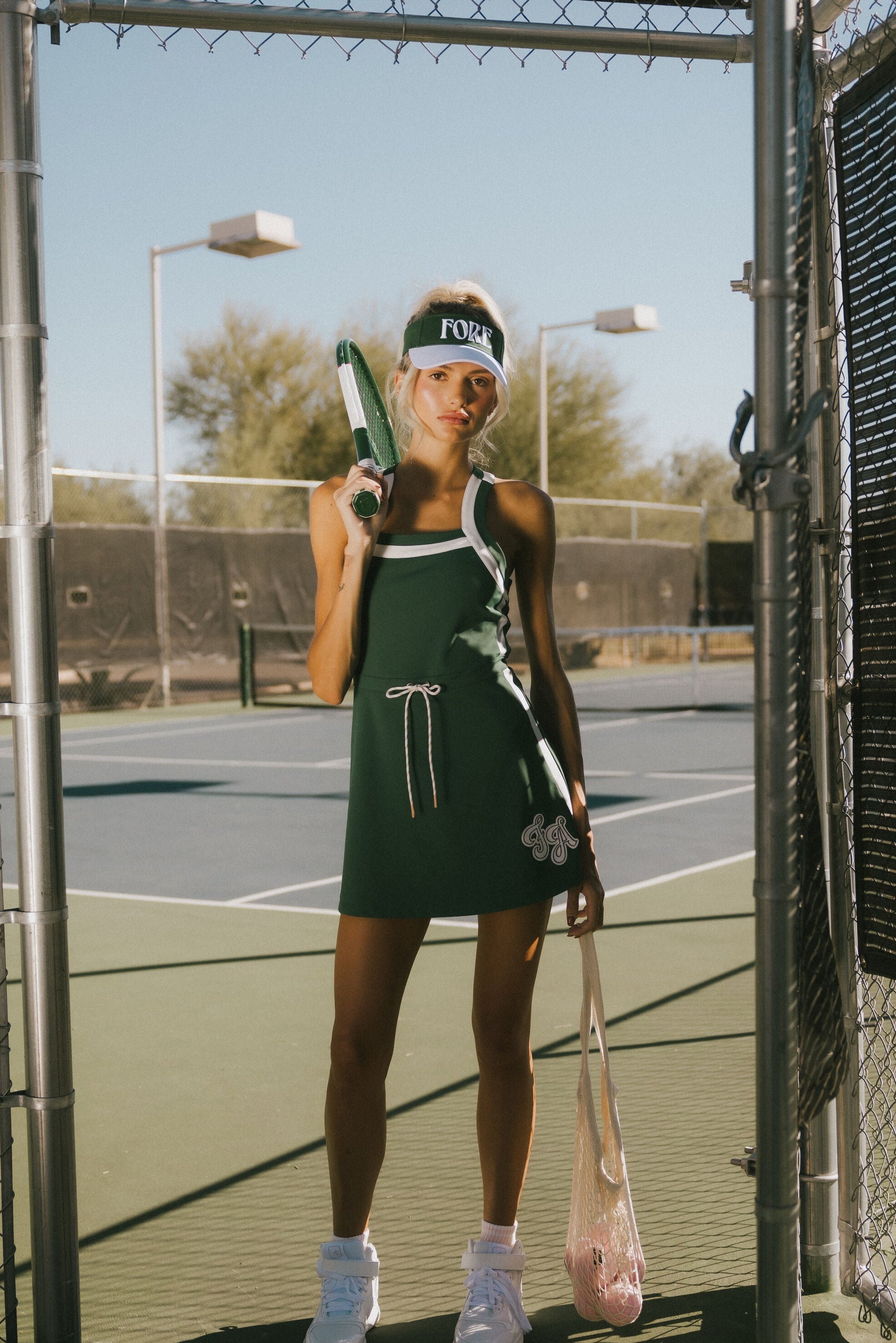 Woman in a green dress holding tennis rackets on a tennis court