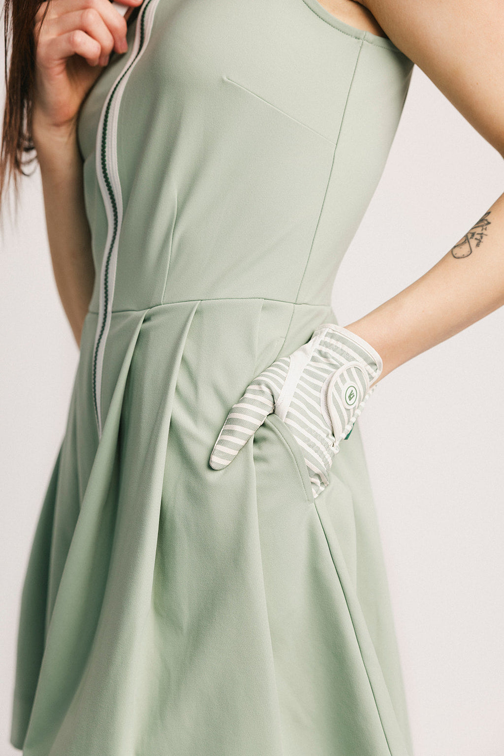 Person wearing a light green dress with a white glove on a plain background