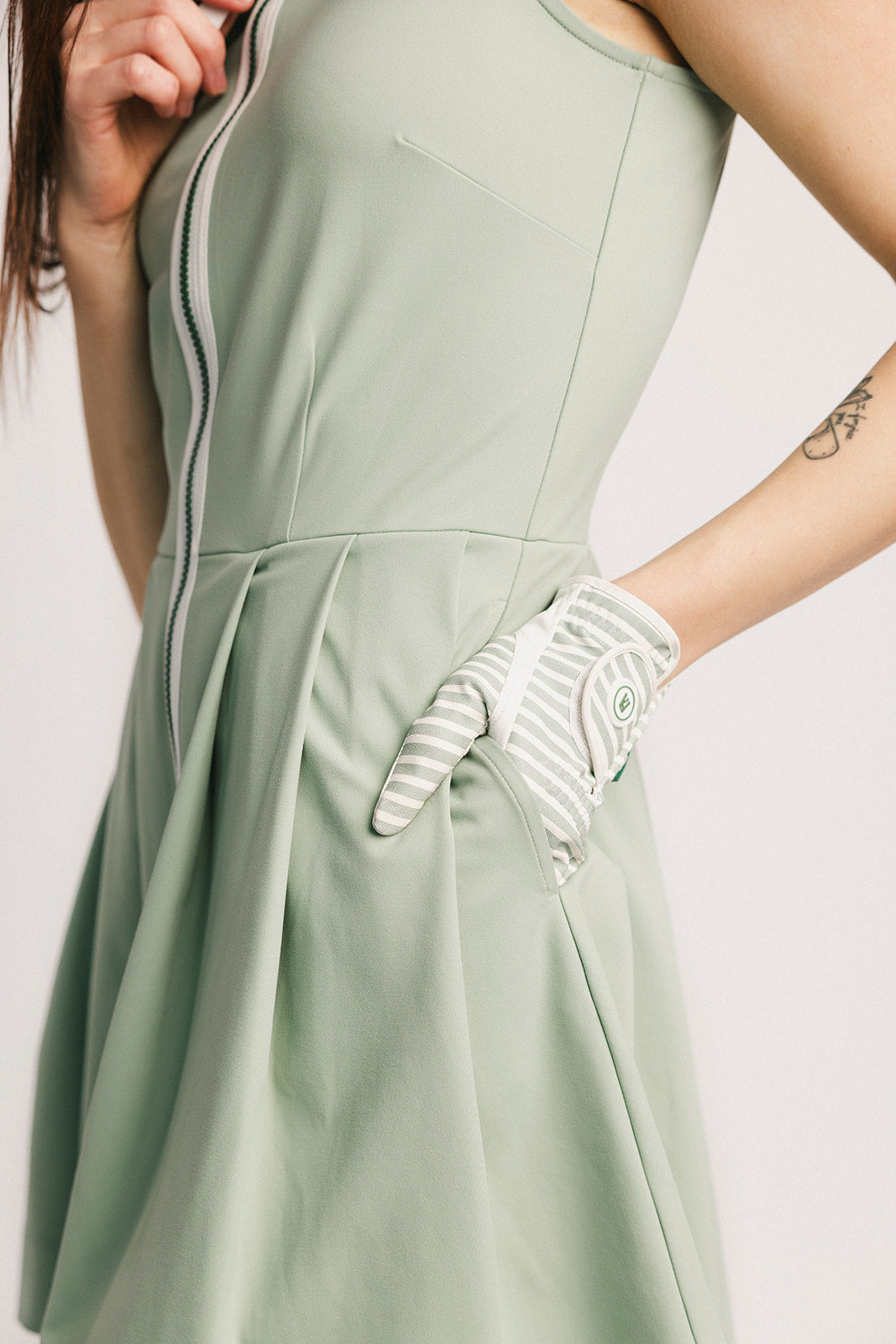 Person wearing a light green dress with a white glove on a plain background