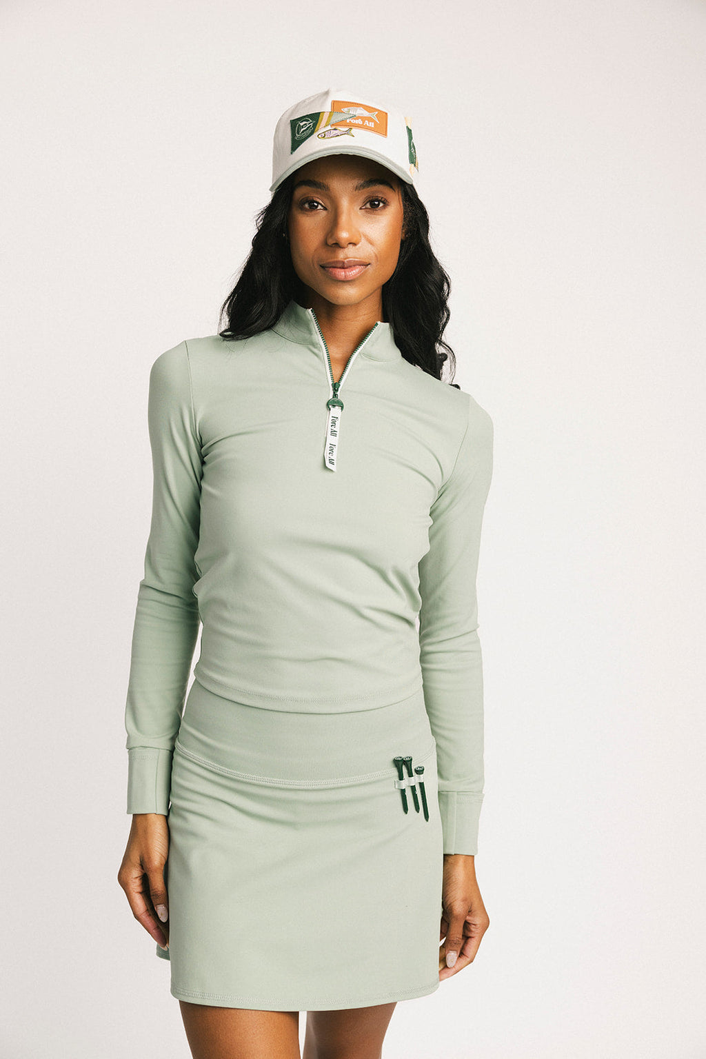 Woman wearing a light green long-sleeve dress and cap on a white background