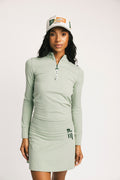 Woman wearing a light green long-sleeve dress and cap on a white background