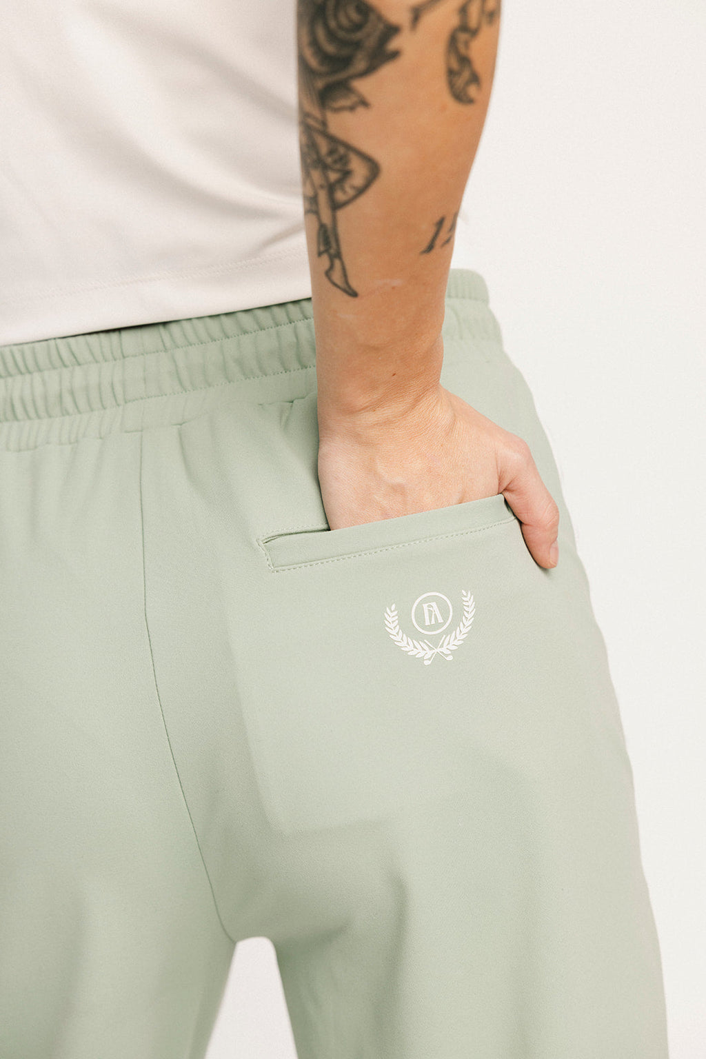 Light green sweatpants with a logo on the pocket worn by a person with tattoos.