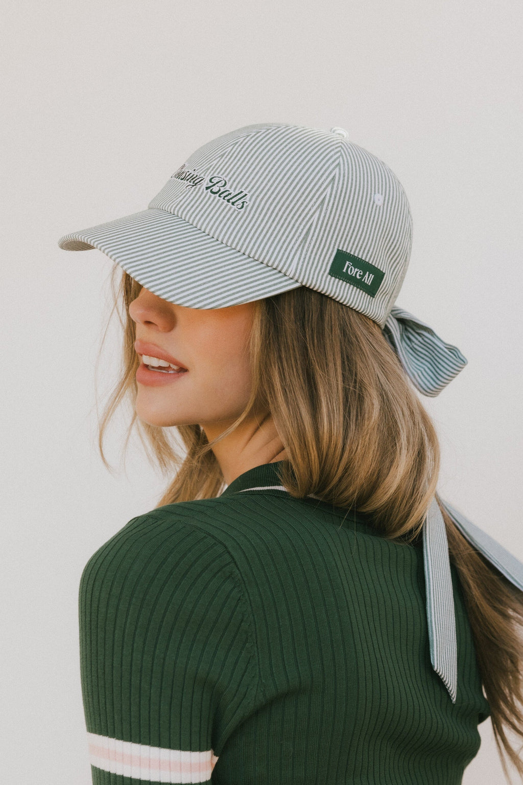 Woman wearing a striped baseball cap and green sweater with white stripes on a plain background