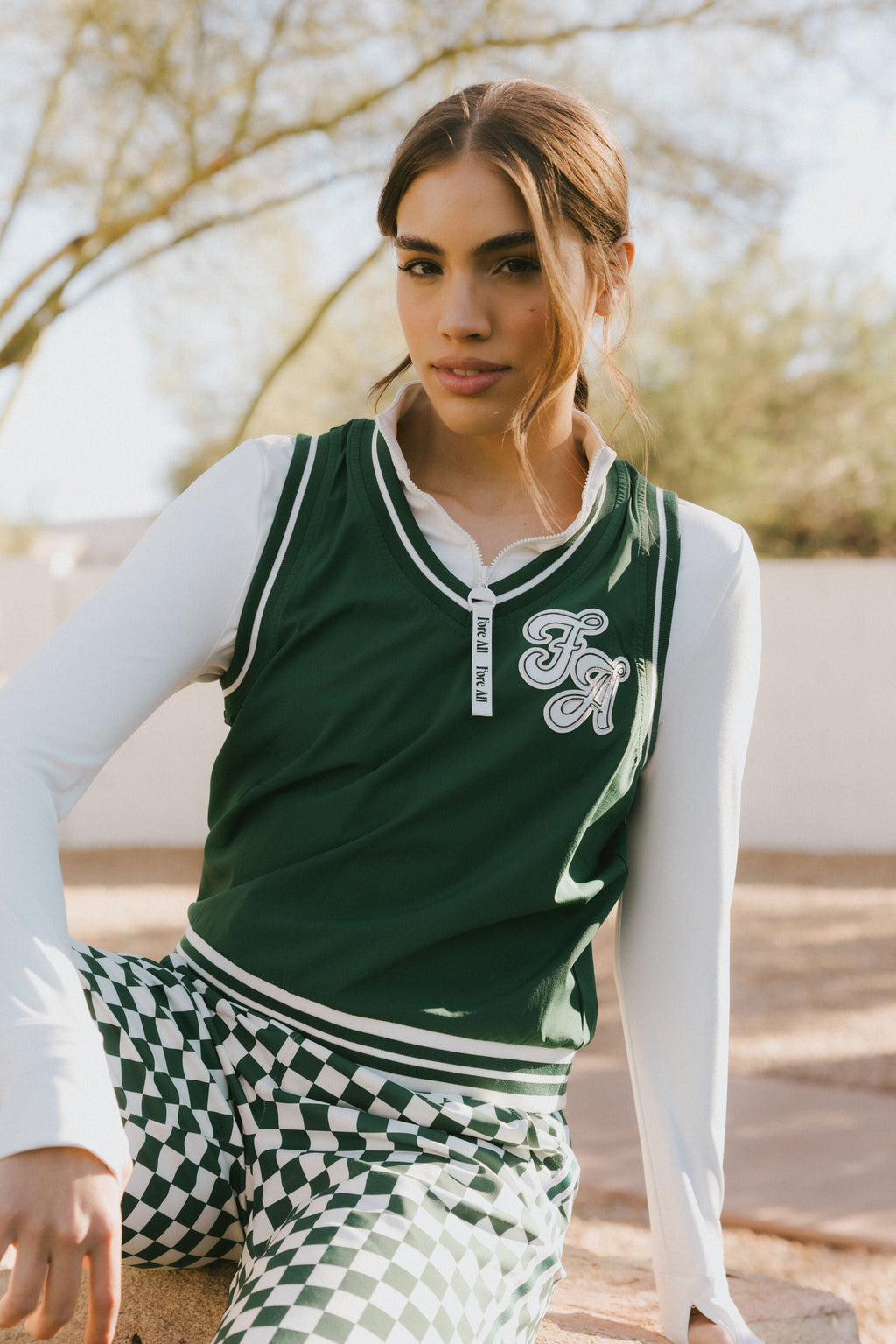 A woman wearing a green sleeveless windbreaker vest with a collar, featuring a white appliquéd logo on the left chest and silicone logos on the upper back.