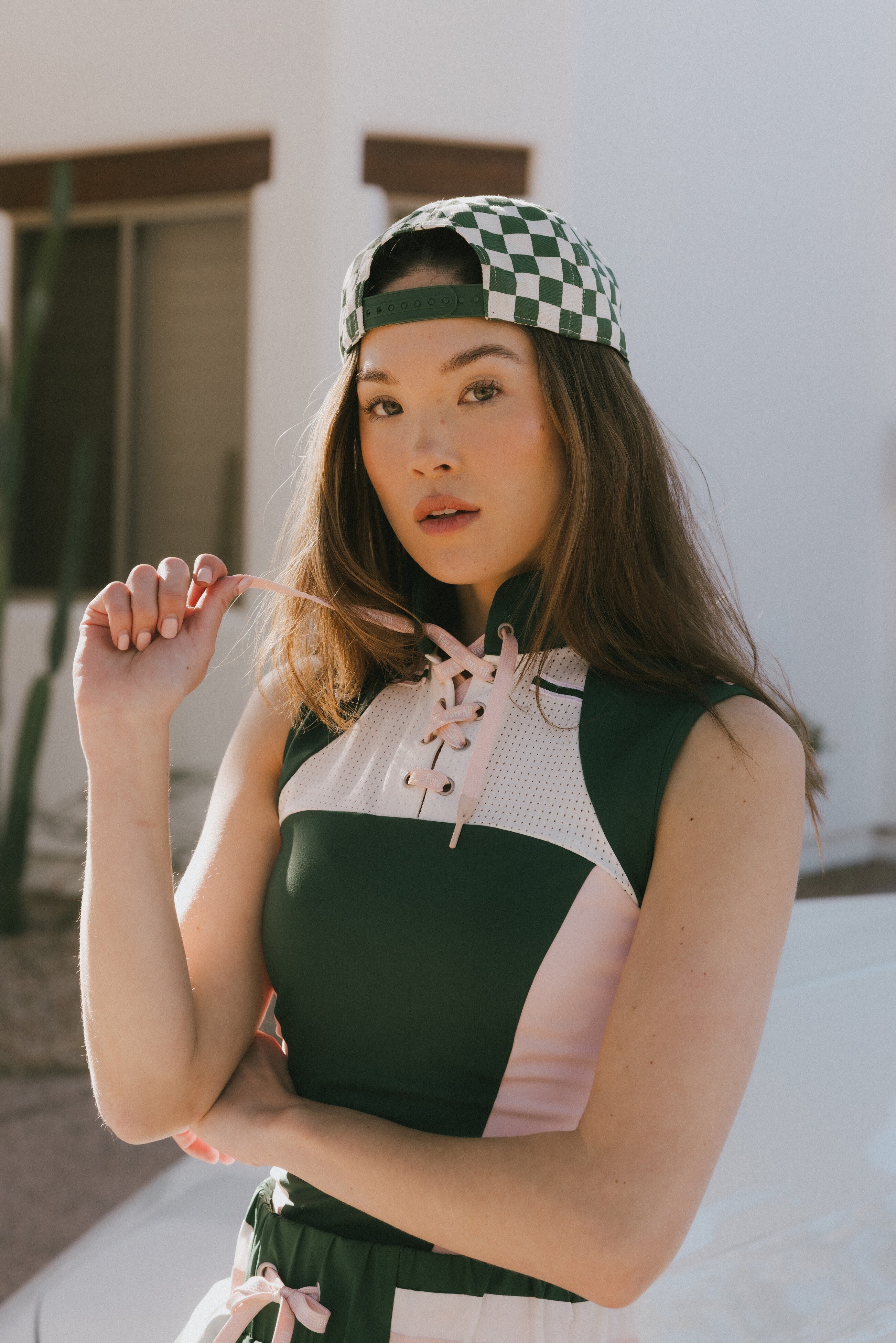 A female model wearing a sleeveless green and pink colorblocked mock neck top with mesh accents and a flat drawstring cord.
