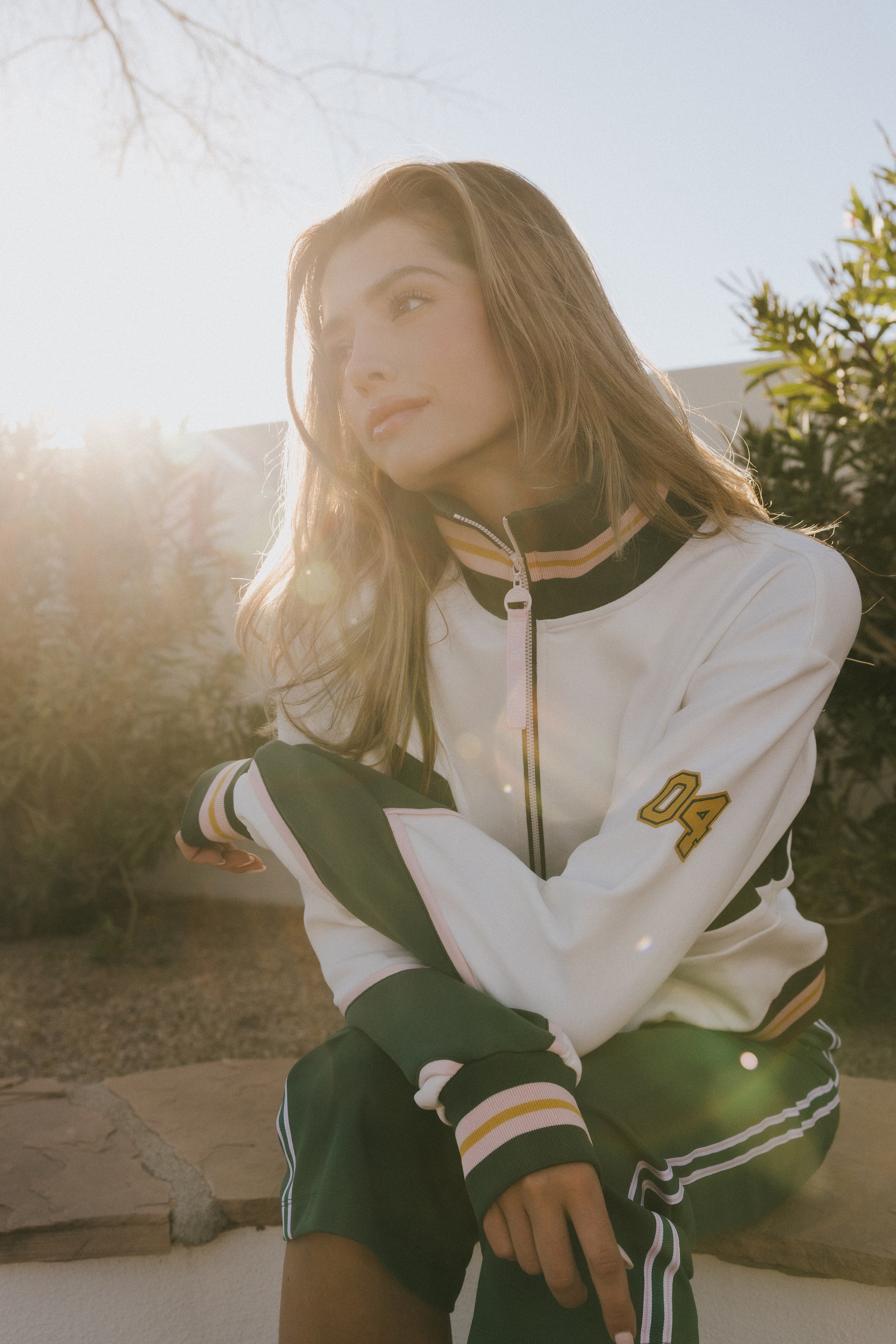 A model wearing the vonn half zip in white sitting on a bench with plants in the background.
