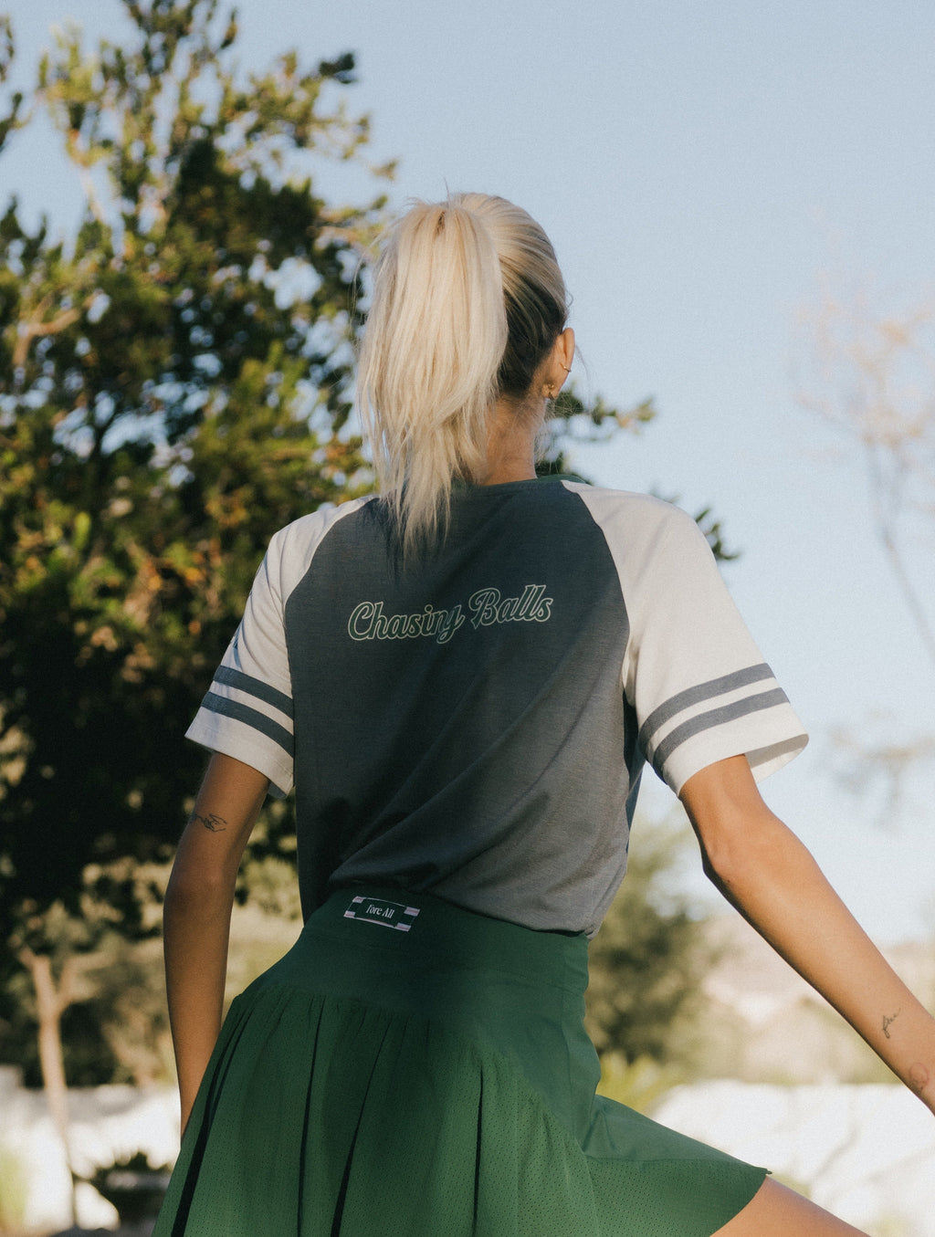 A woman wearing a blue and white striped t-shirt with the words 'chasing balls' on it, paired with a green skirt.