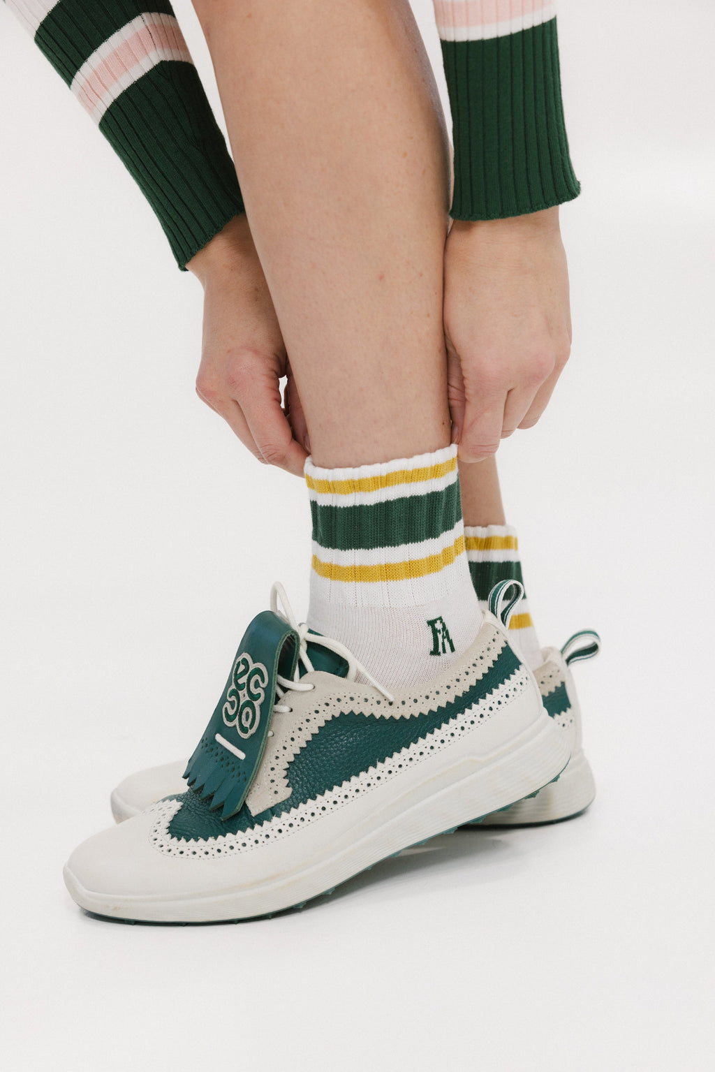 A person wearing retro ankle socks in mustard and green colors, paired with a green and white shoe.