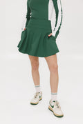 A person wearing a high-waisted green skirt with a solid pattern, paired with a white top and light-colored shoes.
