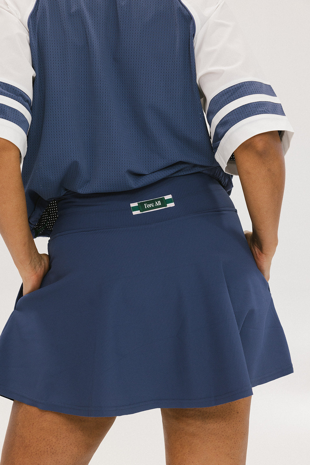 A person wearing a navy-colored knee-length skirt with a high waistband, paired with a golf club themed t-shirt and white sneakers.