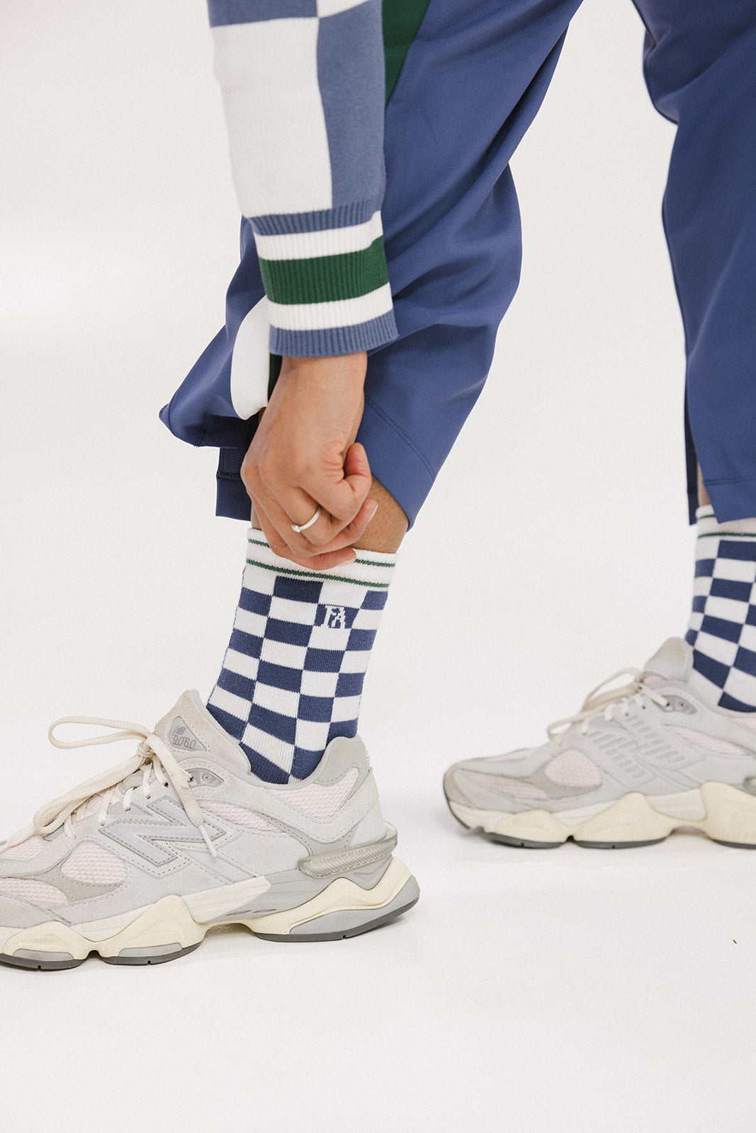 A person wearing indigo and white checkered Charlie Crew Socks with white sneakers and colorful pants.