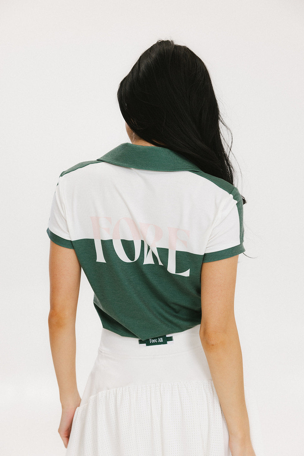 A woman wearing a color block green polo shirt with white front and back yoke detailing, paired with a white skirt.