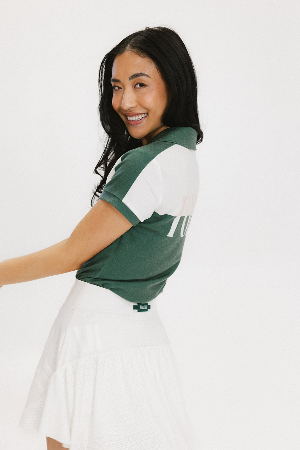 A woman wearing a color block green polo shirt with white front and back yoke detailing, paired with a white skirt.