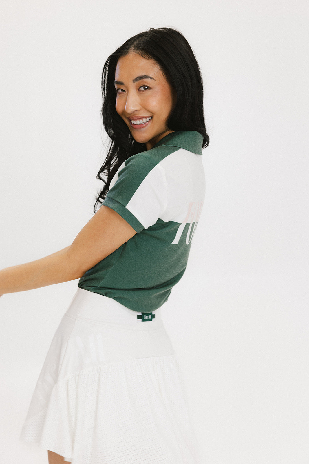A woman wearing a color block green polo shirt with white front and back yoke detailing, paired with a white skirt.