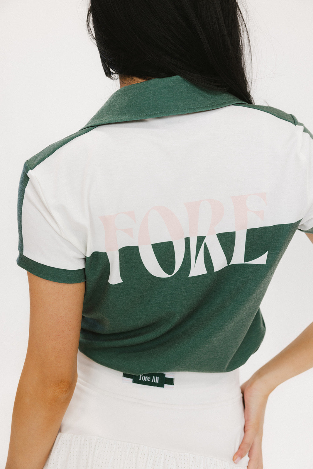 A woman wearing a color block green polo shirt with white front and back yoke detailing, paired with a white skirt.