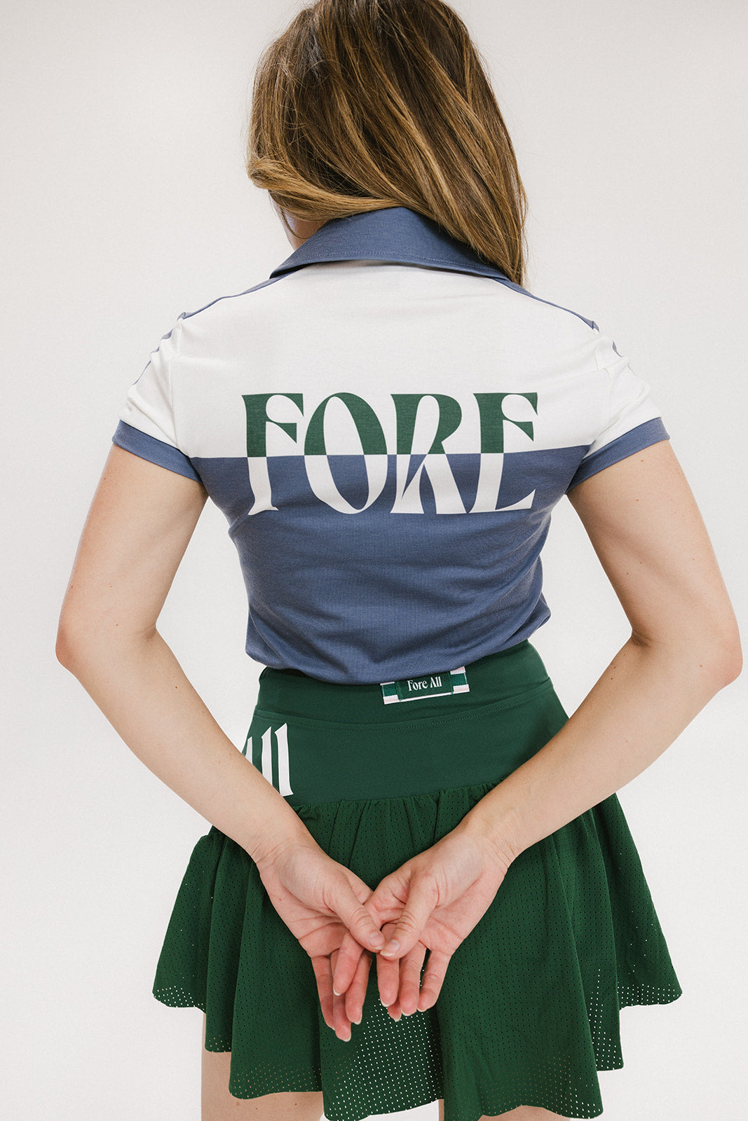 A woman wearing a color block indigo polo shirt with front and back yoke detailing, paired with a green skirt.