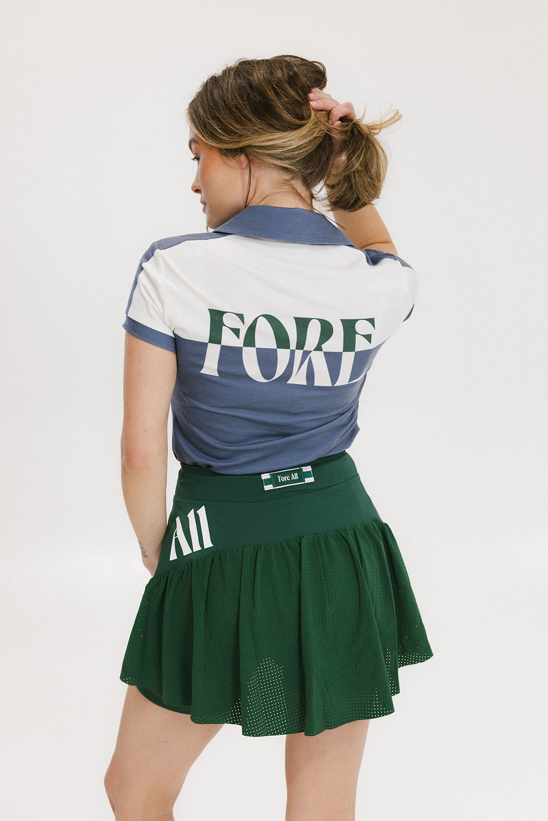 A woman wearing a color block indigo polo shirt with front and back yoke detailing, paired with a green skirt.
