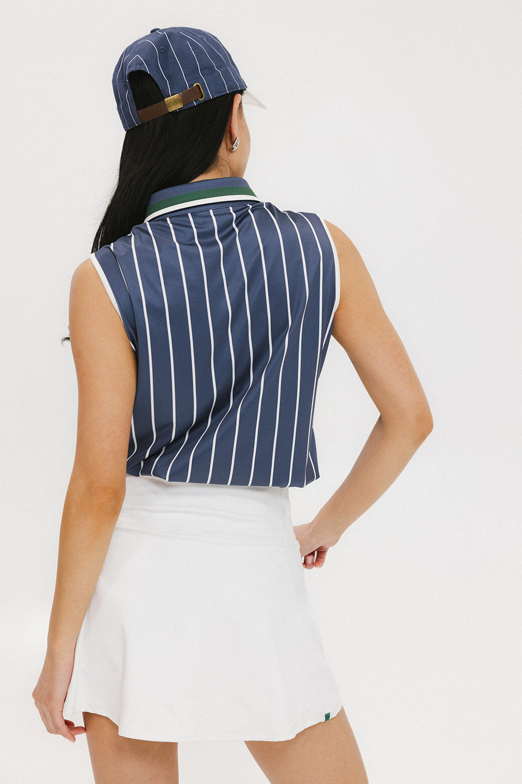 A woman wearing a sleeveless navy blue and white striped Moore Polo golf top with a cap and a white skirt.