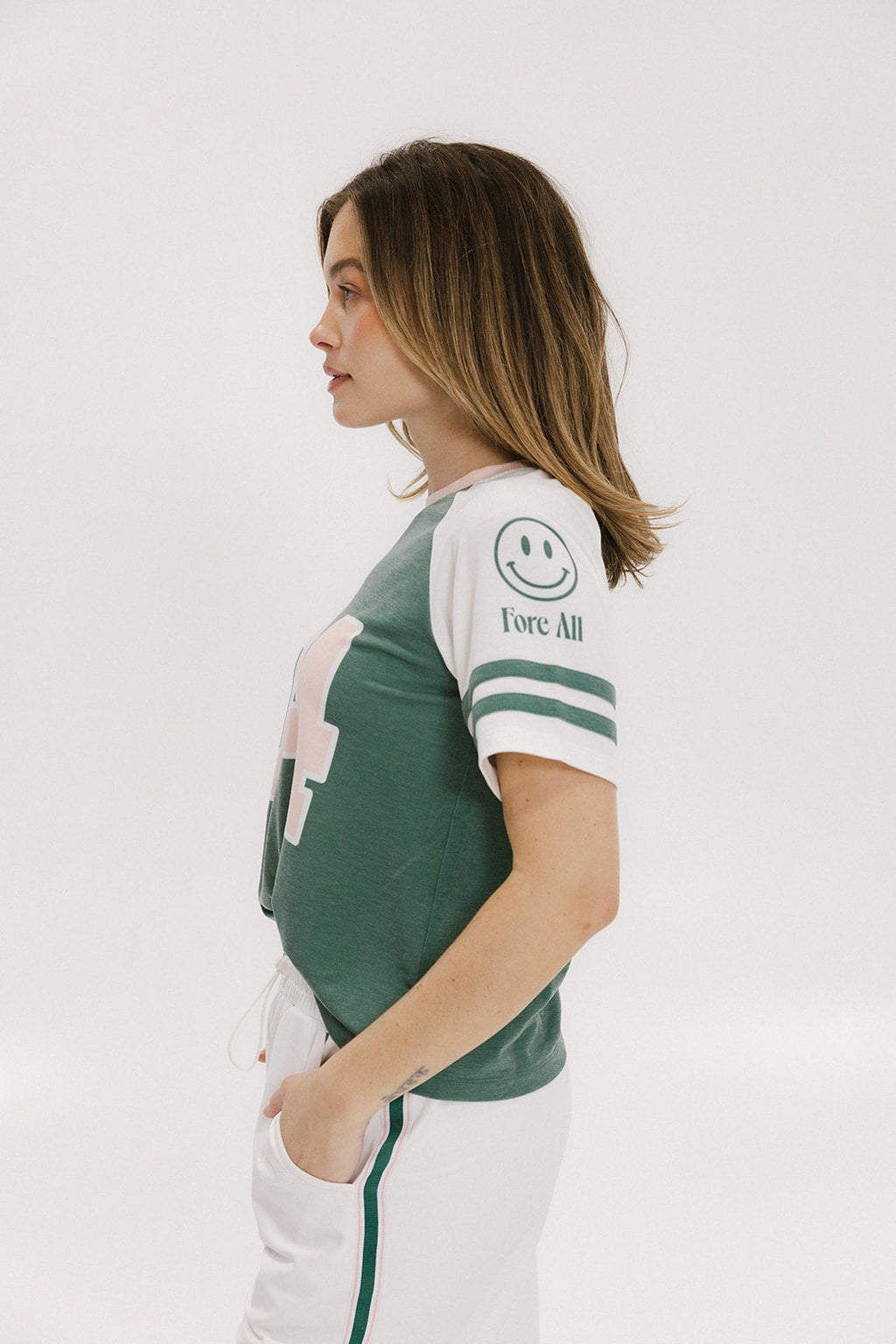 A woman wearing a green and white boxy fit t-shirt with the number 04 on the front and bold lettering on the back, along with striped sleeves.