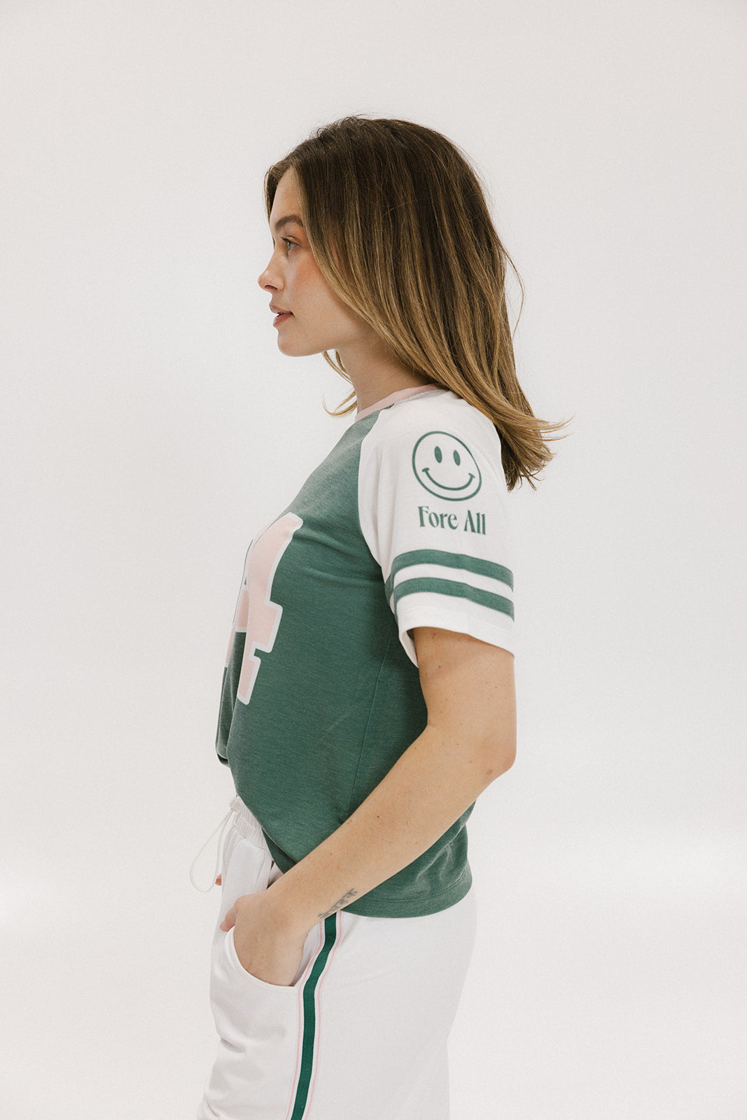 A woman wearing a green and white boxy fit t-shirt with the number 04 on the front and bold lettering on the back, along with striped sleeves.
