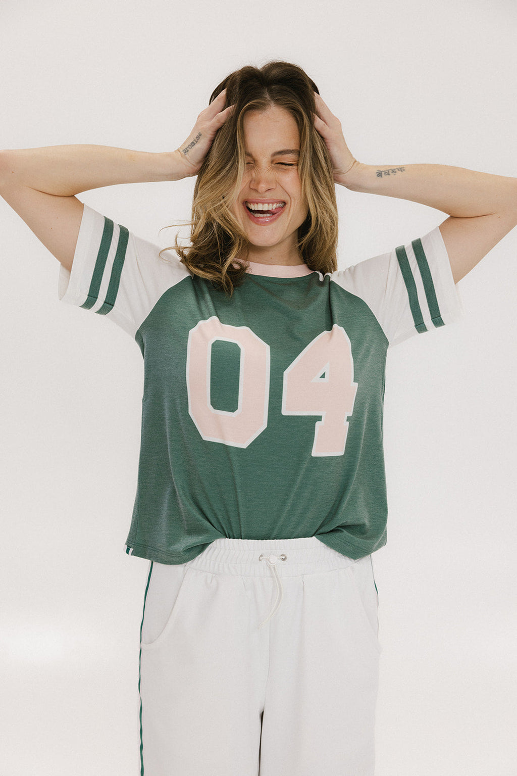A woman wearing a green and white boxy fit t-shirt with the number 04 on the front and bold lettering on the back, along with striped sleeves.