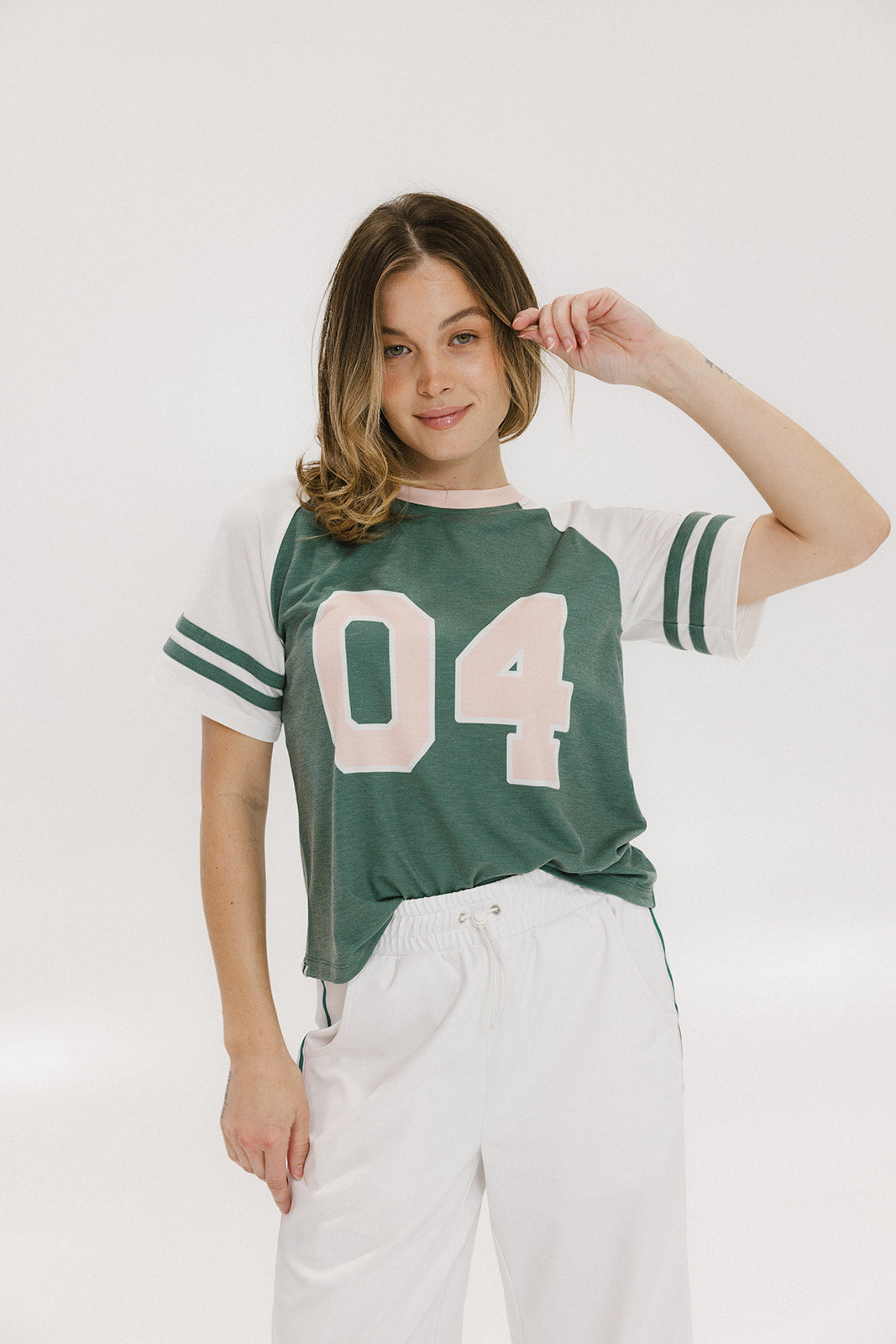 A woman wearing a green and white boxy fit t-shirt with the number 04 on the front and bold lettering on the back, along with striped sleeves.