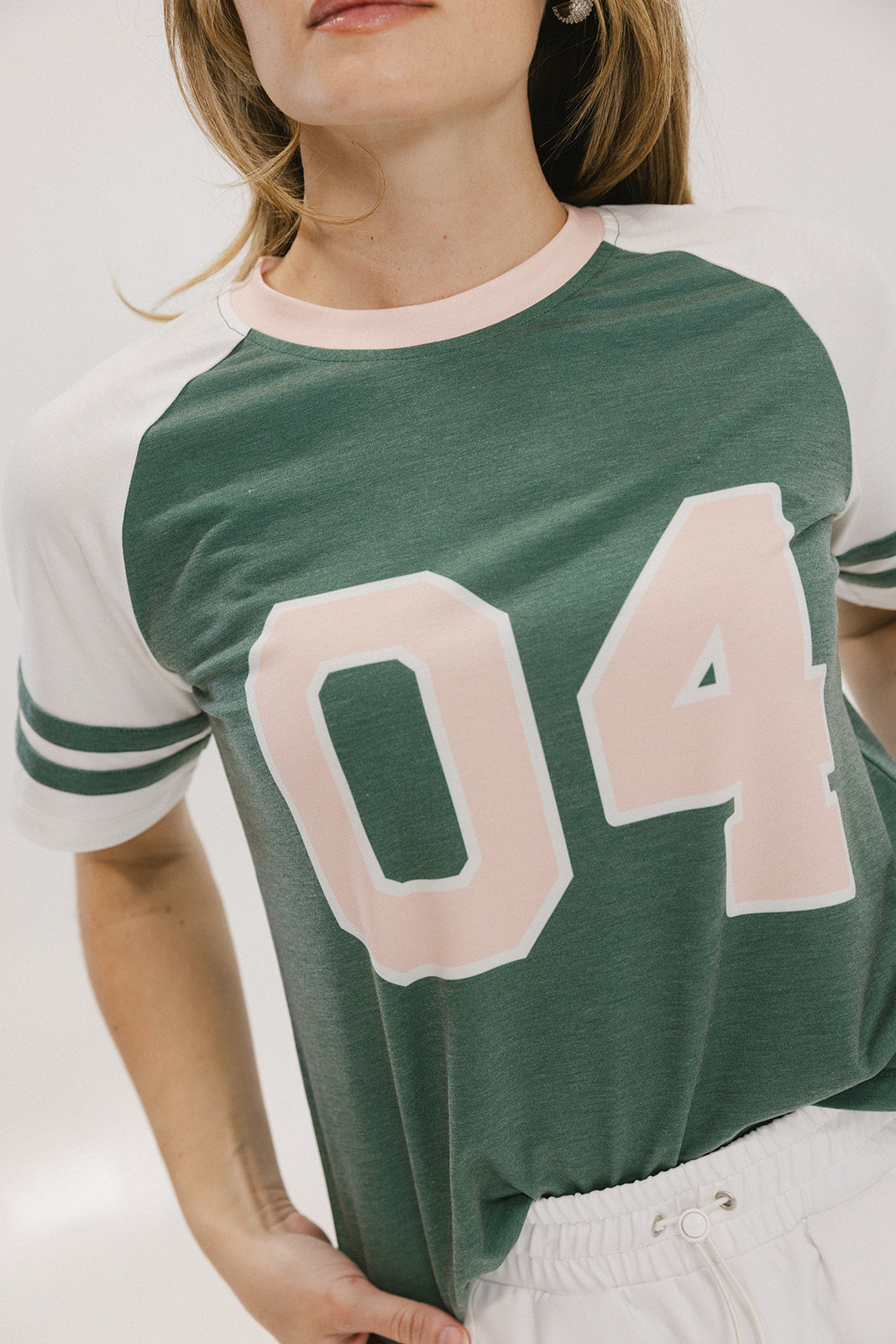 A woman wearing a green and white boxy fit t-shirt with the number 04 on the front and bold lettering on the back, along with striped sleeves.