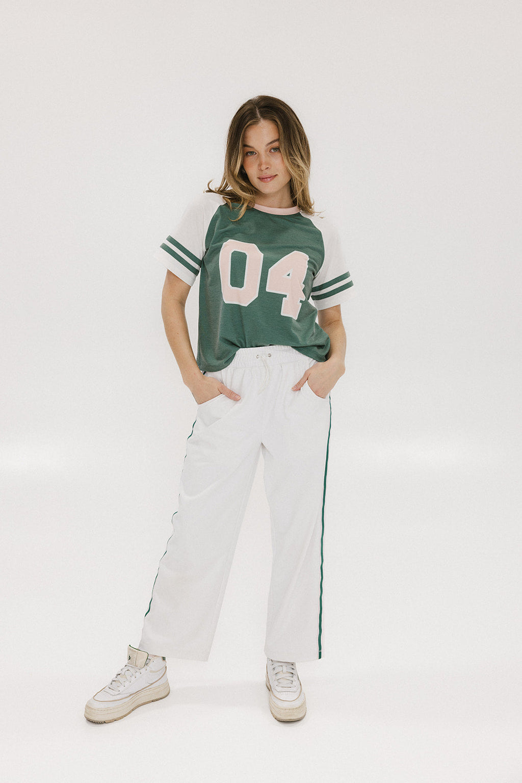 A woman wearing a green and white boxy fit t-shirt with the number 04 on the front and bold lettering on the back, along with striped sleeves.