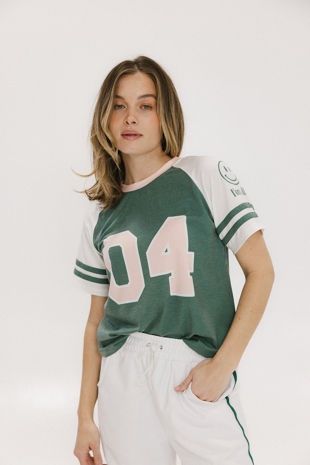 A woman wearing a green and white boxy fit t-shirt with the number 04 on the front and bold lettering on the back, along with striped sleeves.