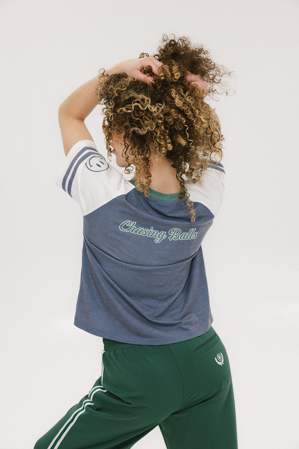 A woman wearing a blue and white striped t-shirt with the words 'chasing balls' on it, paired with green pants.