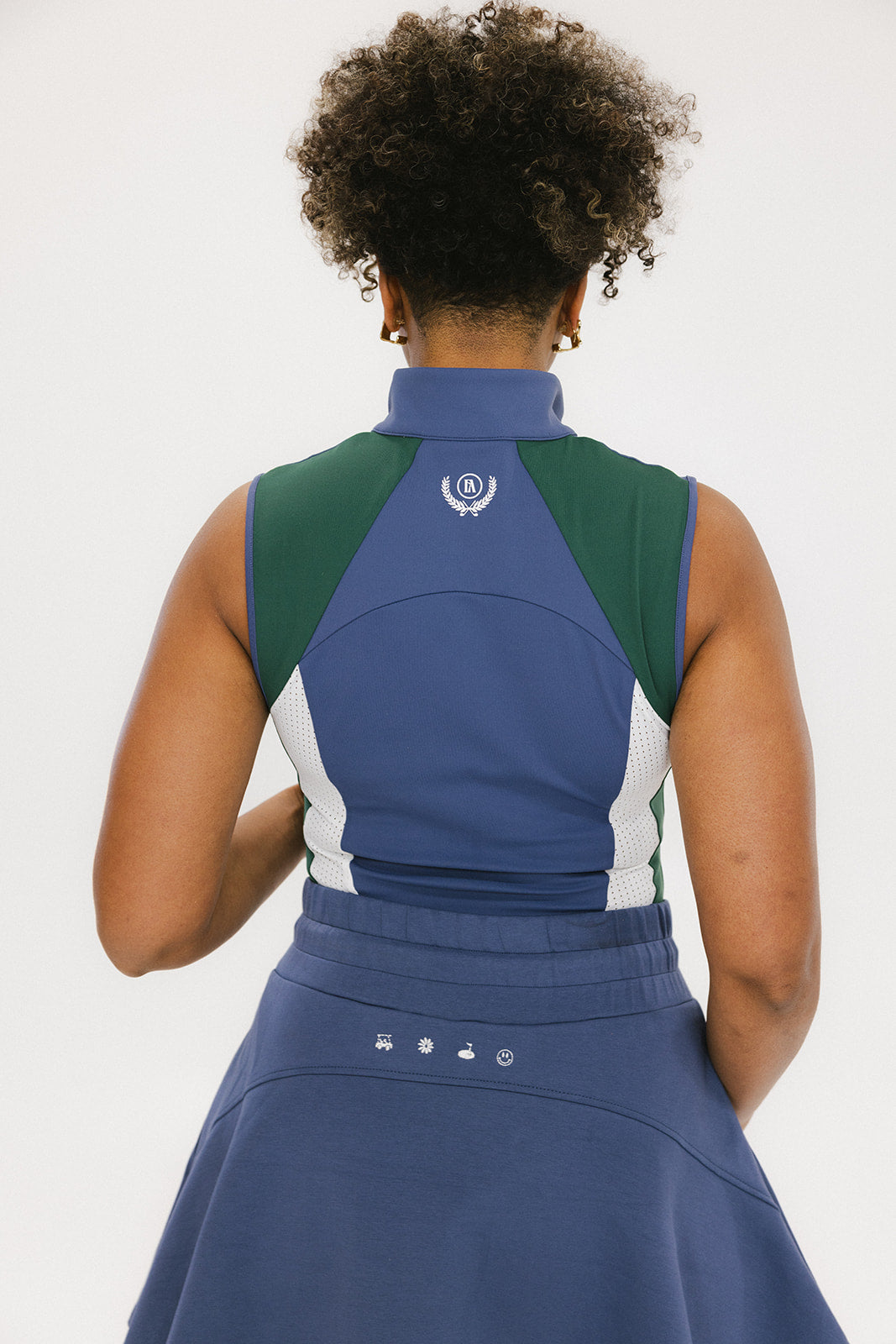 A woman wearing a sleeveless colorblocked mock neck tank top in blue and green with mesh accents and a flat drawstring cord.
