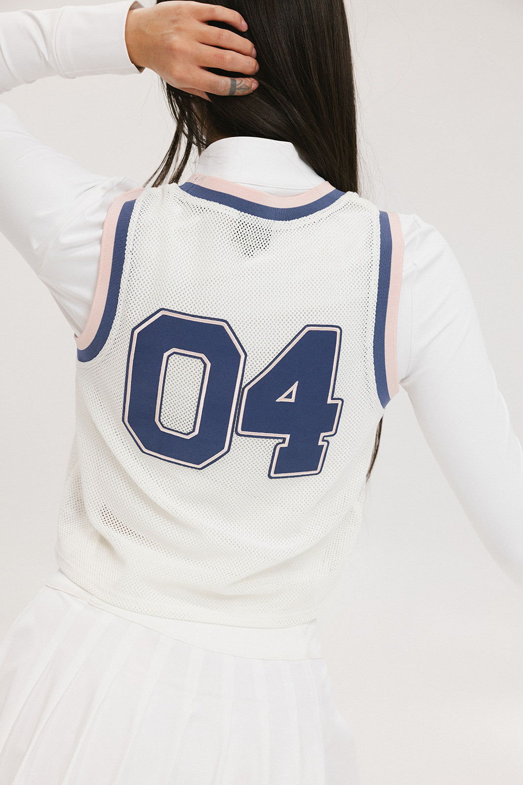 A woman wearing a white sleeveless tank top with '04' text and a flamingo logo on the chest, paired with a white skirt.