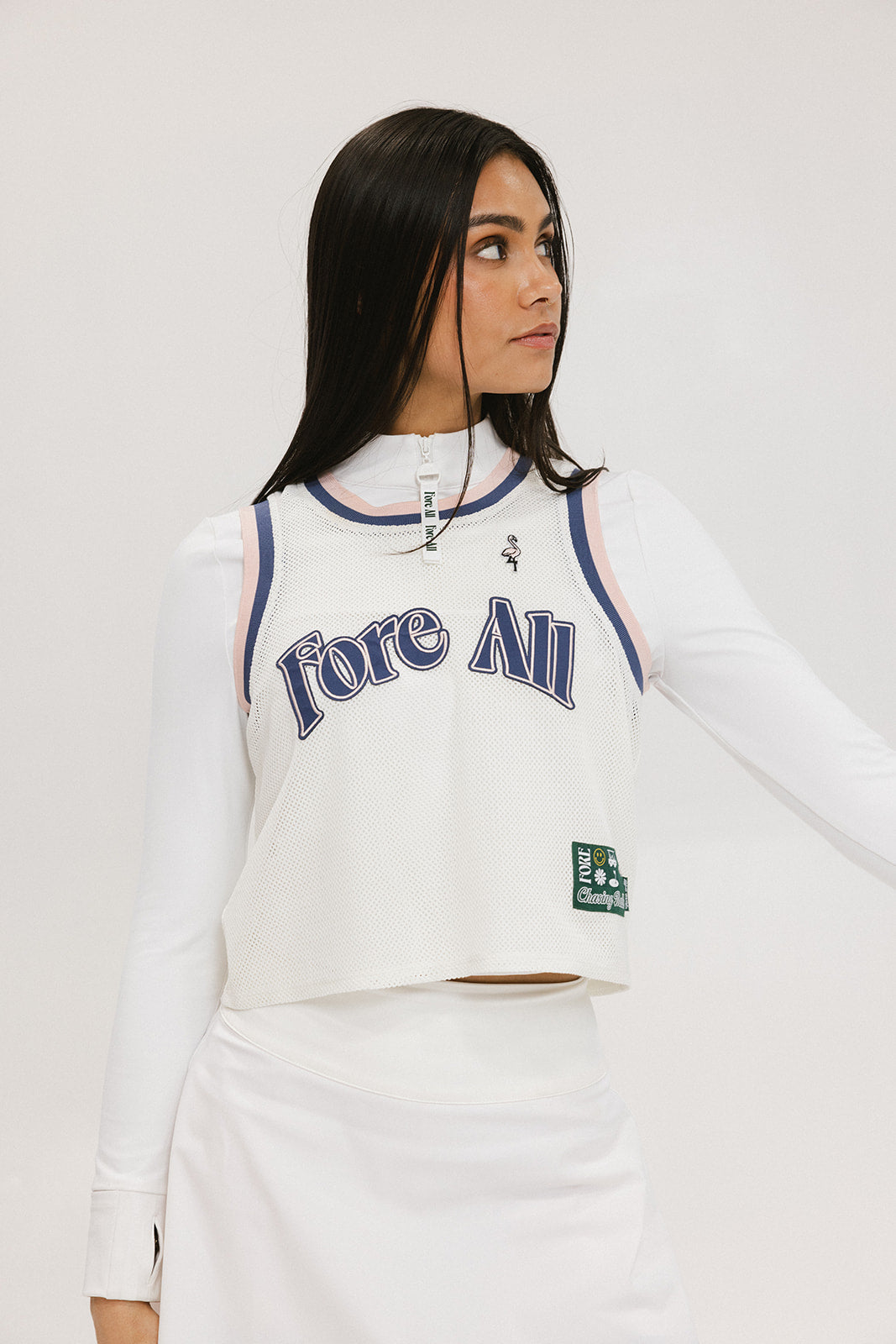 A woman wearing a white sleeveless tank top with 'Fore All' text and a flamingo logo on the chest, paired with a white skirt.