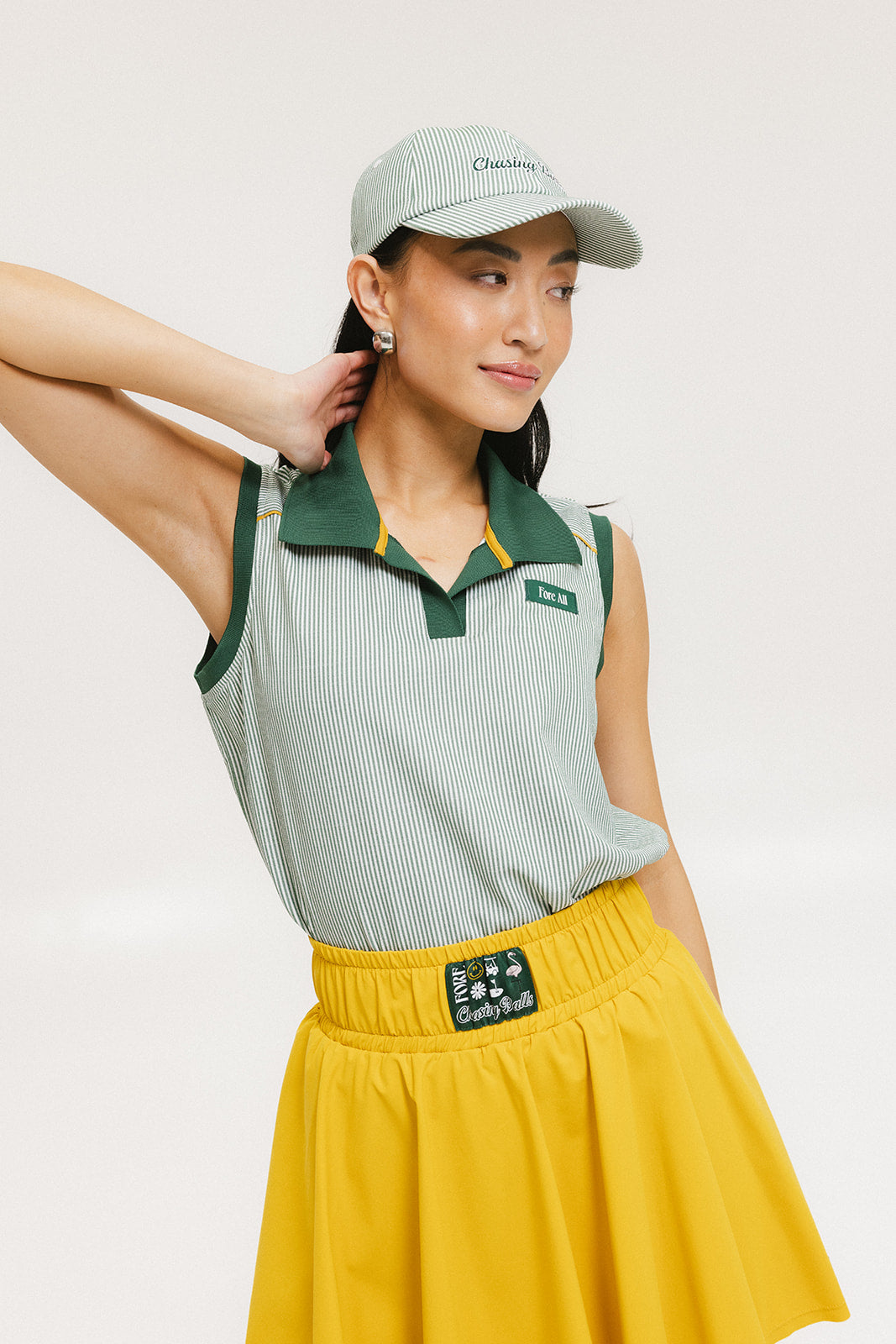 A woman wearing a green striped polo shirt and a matching green cap, with a yellow skirt.
