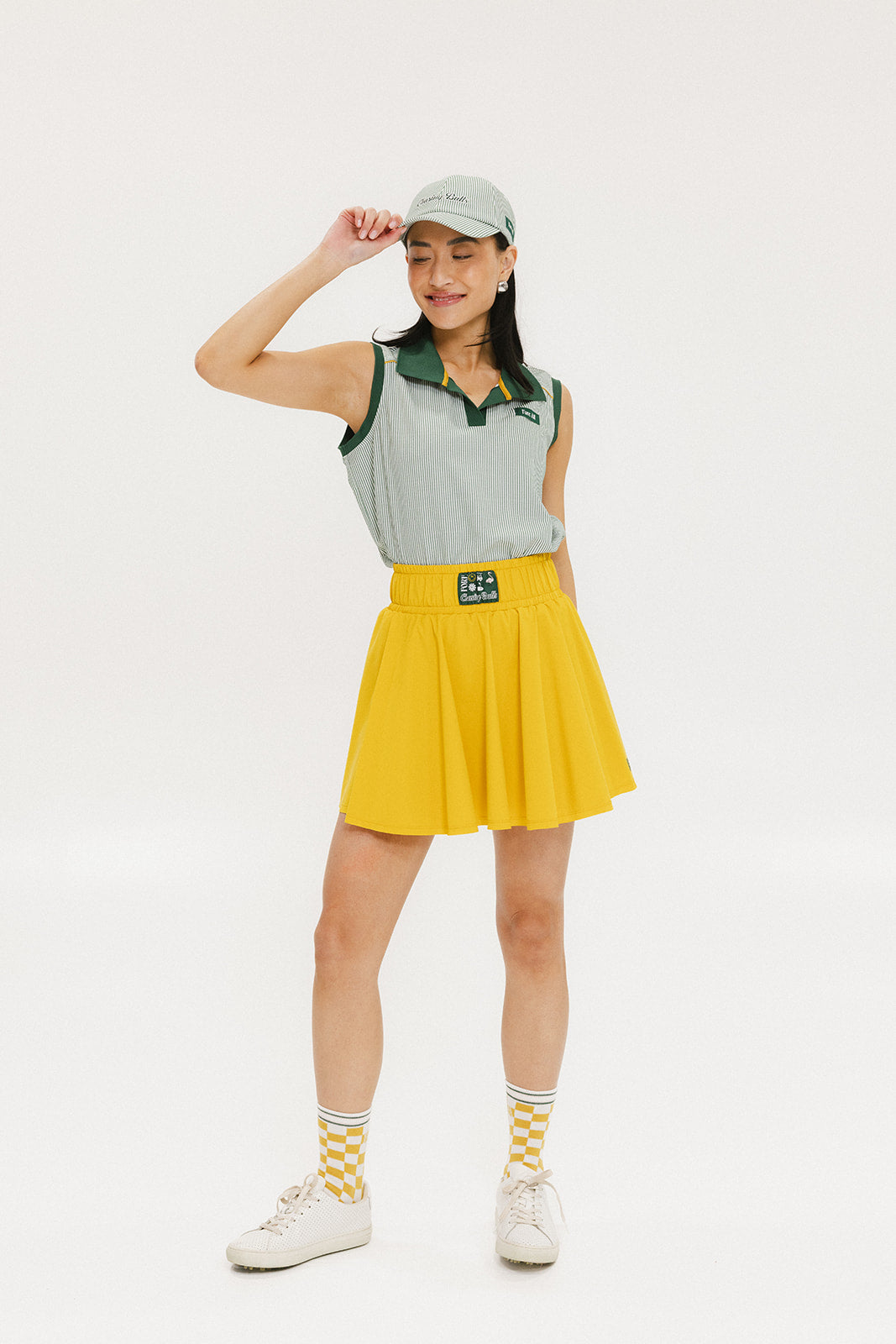 A woman wearing a green striped polo shirt and a matching green cap, with a yellow skirt.
