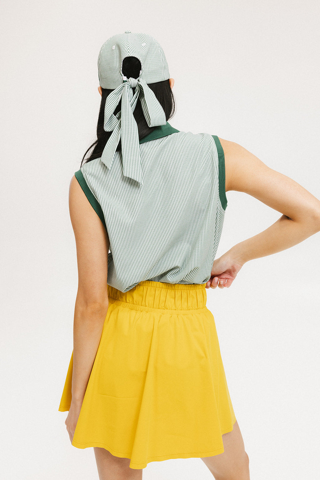 A woman wearing a green striped polo shirt and a matching green cap, with a yellow skirt.