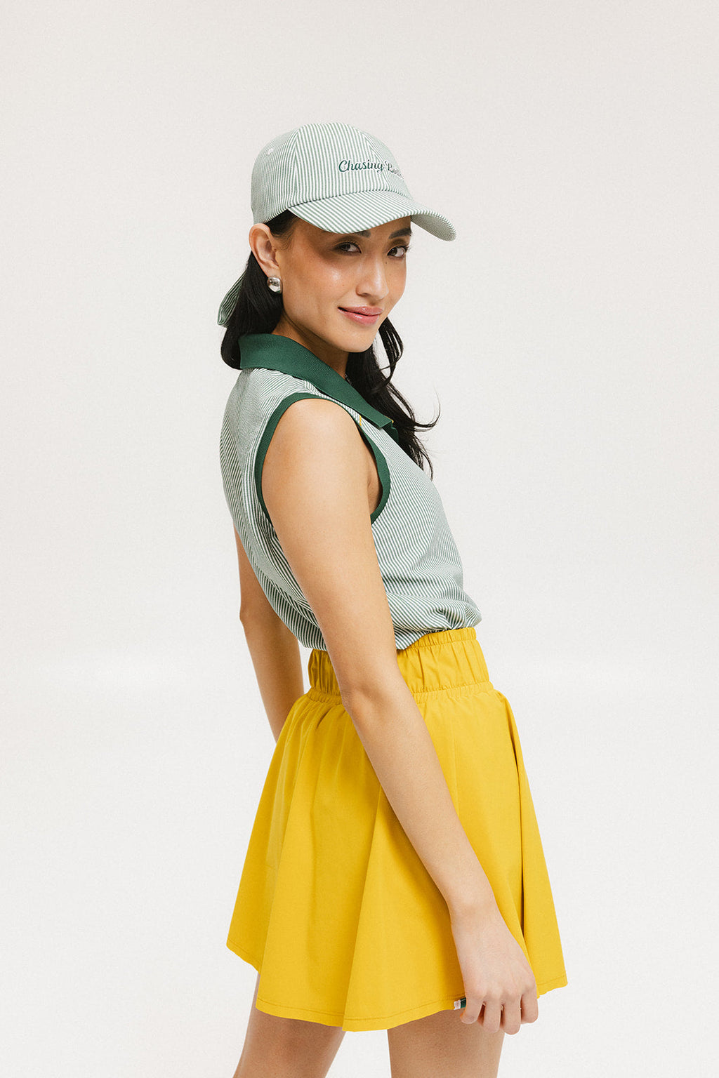 A woman wearing a green striped polo shirt and a matching green cap, with a yellow skirt.