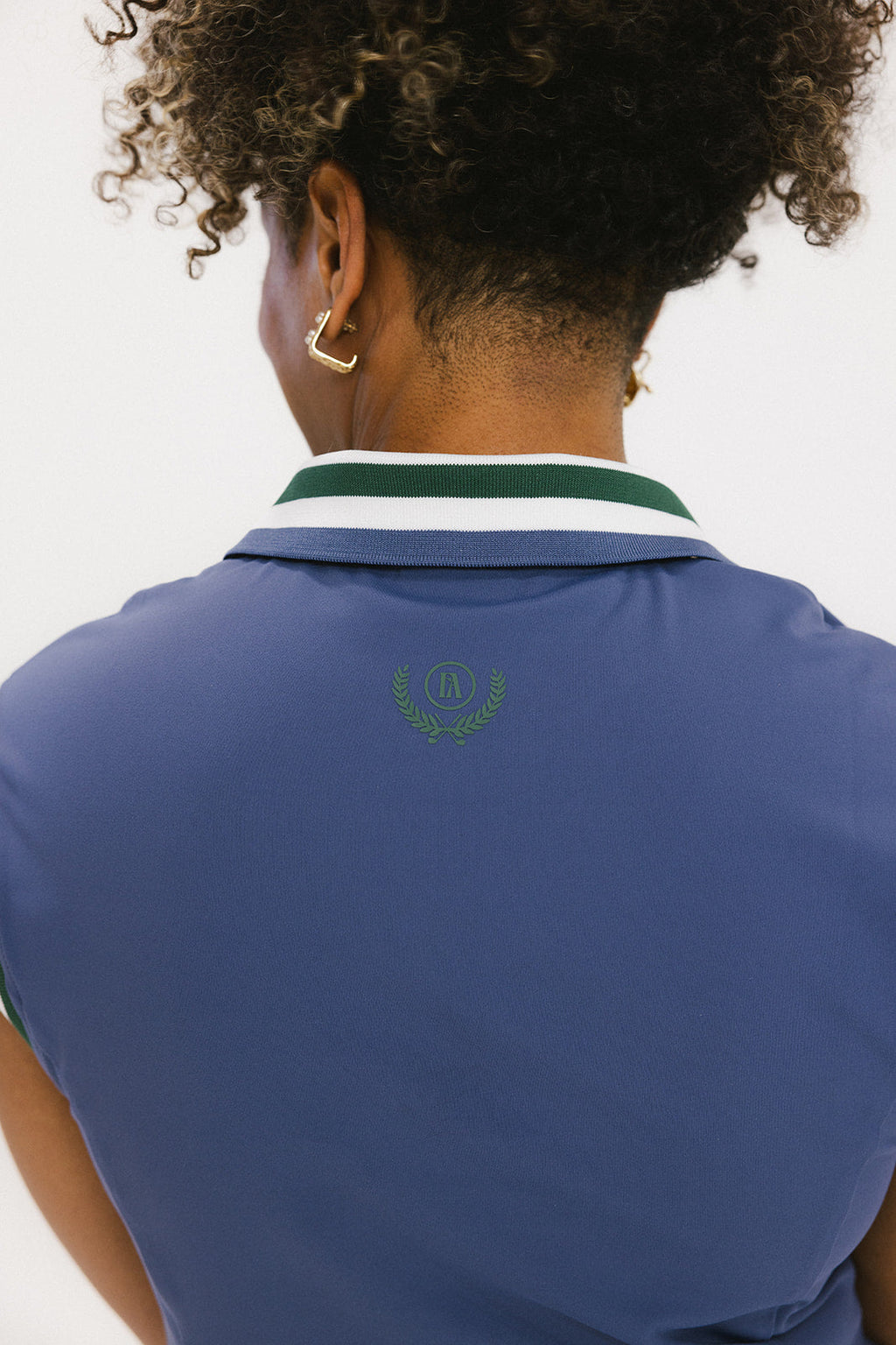 A woman wearing a sleeveless indigo blue polo with a striped collar and v-neck.