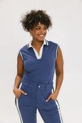 A woman wearing a sleeveless indigo blue polo with a striped collar and v-neck.