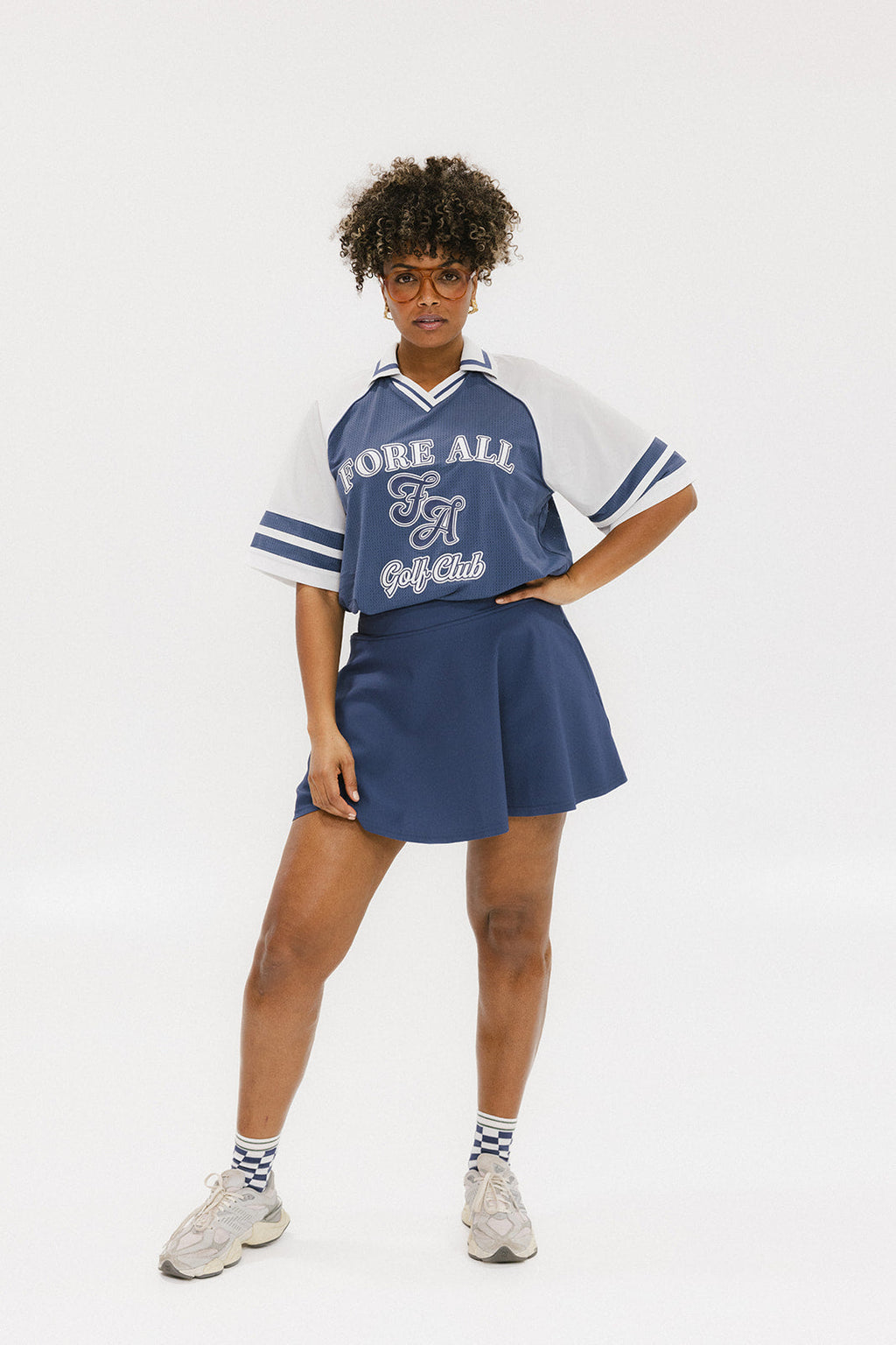 A person wearing a blue and white rugby-inspired polo shirt with Mesh body appliqué logos, a ribbed collar and placket, and elastic toggles at the side seam hem. The shirt has 'FORE ALL' text and a golf club logo on the front.