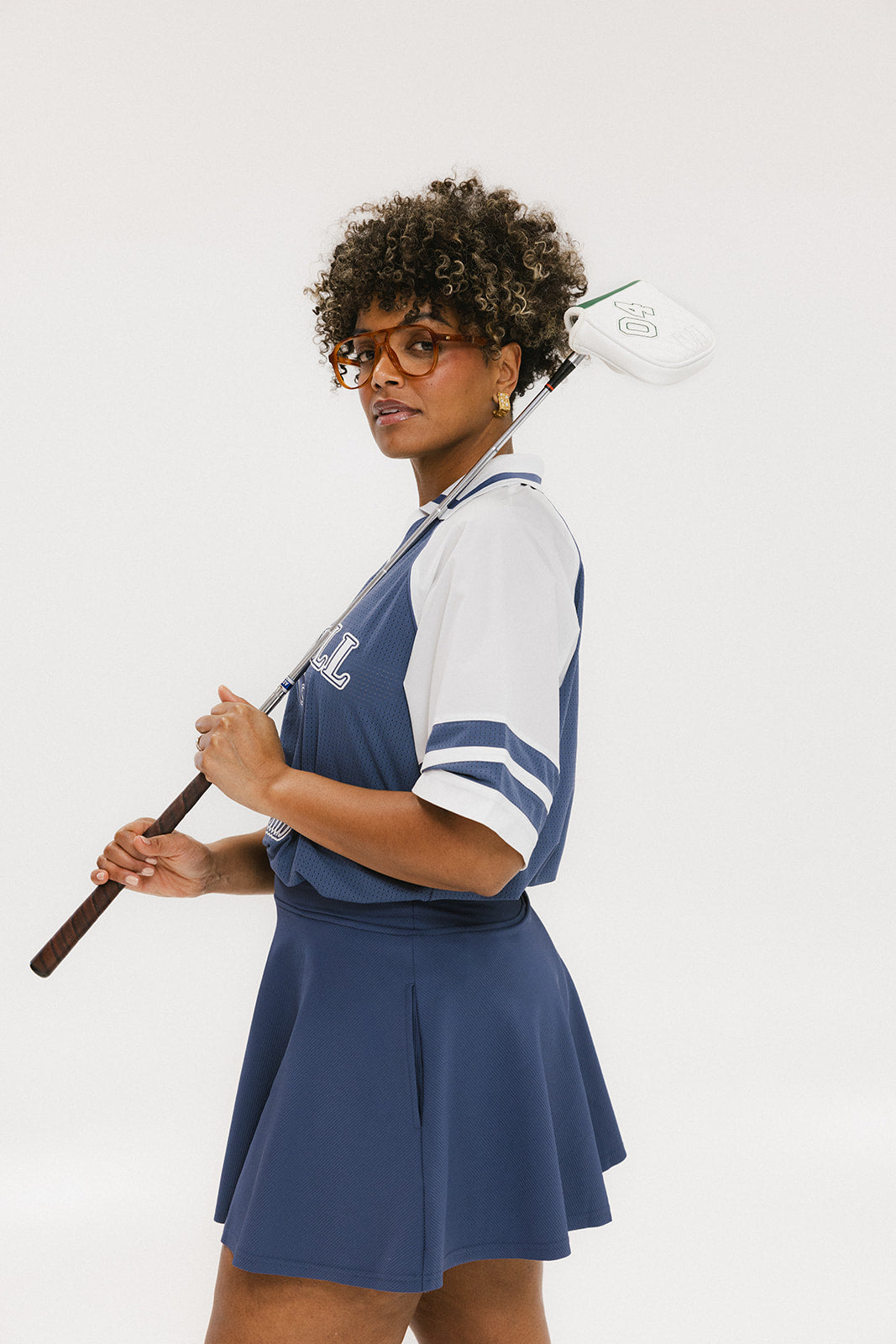 A person wearing a blue and white rugby-inspired polo shirt with Mesh body appliqué logos, a ribbed collar and placket, and elastic toggles at the side seam hem. The shirt has 'FORE ALL' text and a golf club logo on the front.