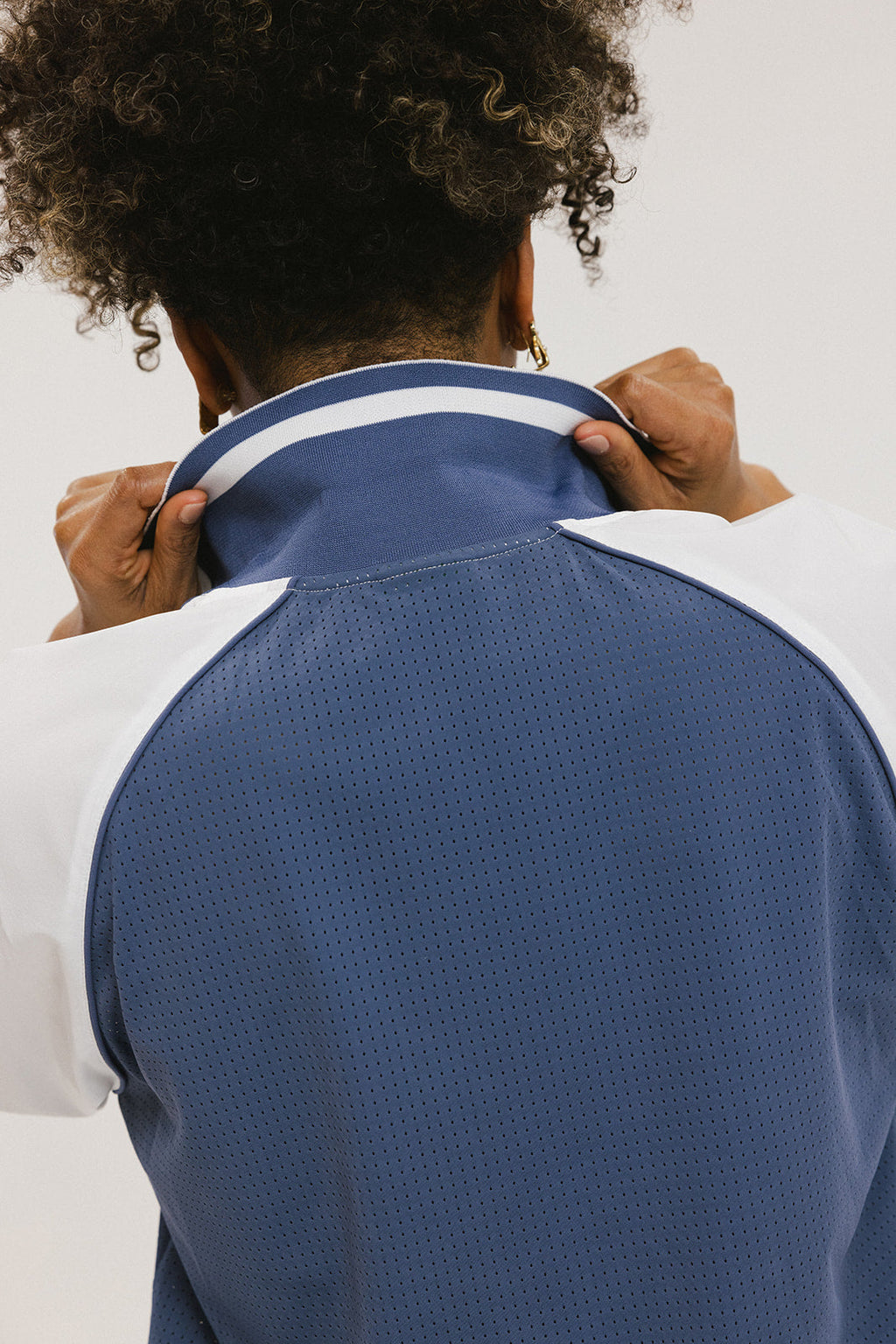 A person wearing a blue and white rugby-inspired polo shirt with Mesh body appliqué logos, a ribbed collar and placket, and elastic toggles at the side seam hem. The shirt has 'FORE ALL' text and a golf club logo on the front.