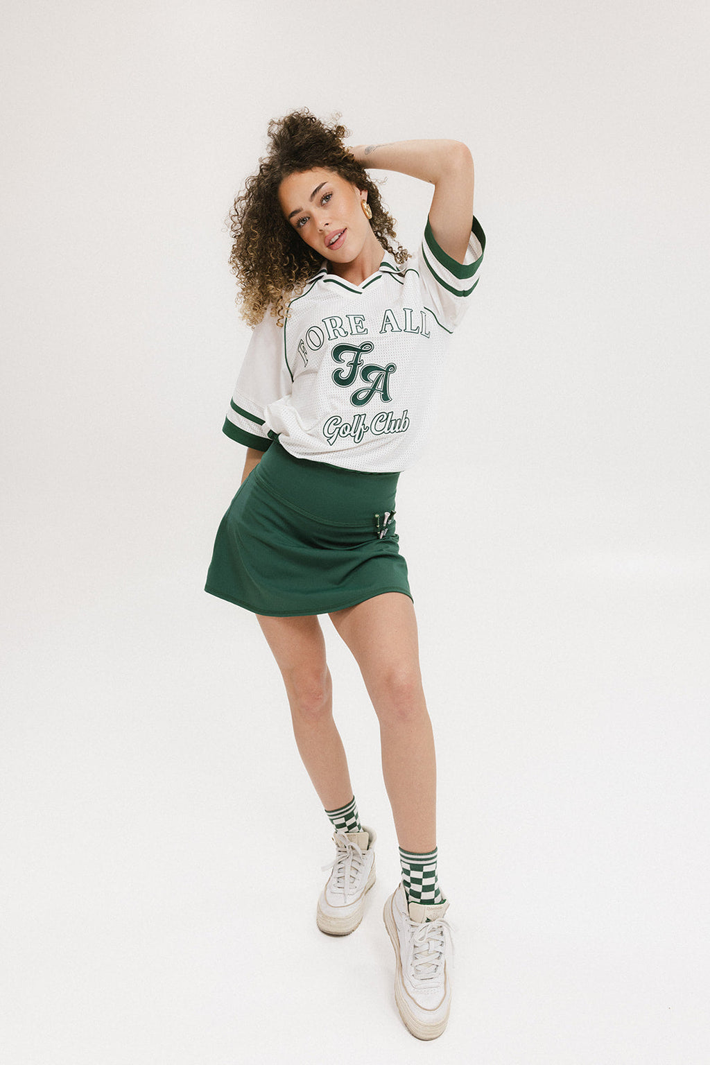 A woman wearing a white rugby-inspired polo shirt with green details and text that reads 'FORE Golf Club'.