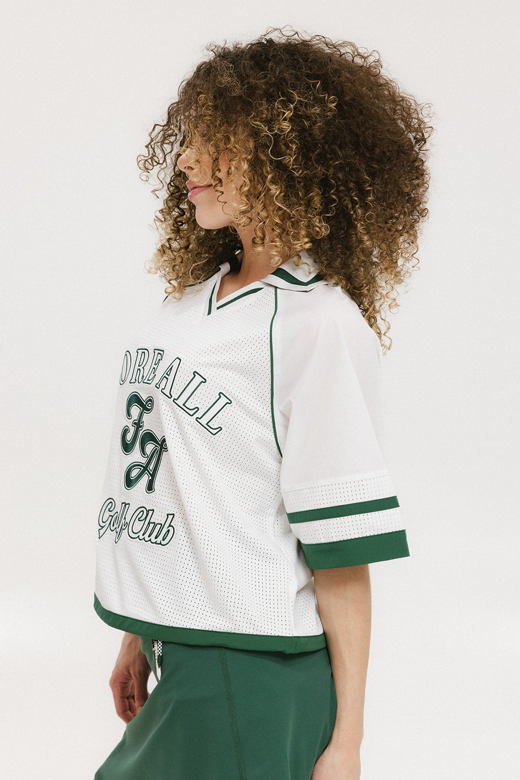A woman wearing a white rugby-inspired polo shirt with green details and text that reads 'FORE Golf Club'.