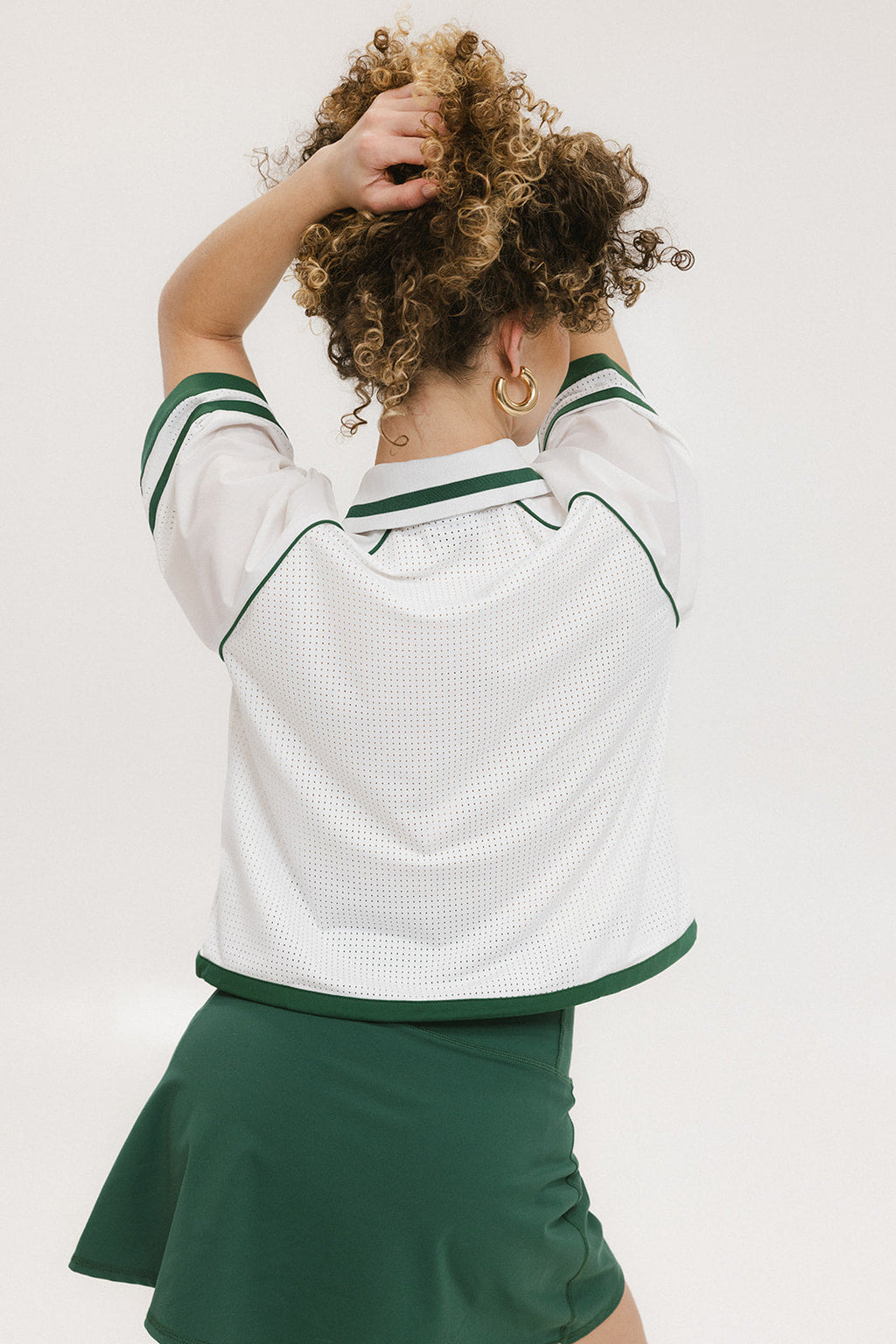 A woman wearing a white rugby-inspired polo shirt with green details and text that reads 'FORE Golf Club'.