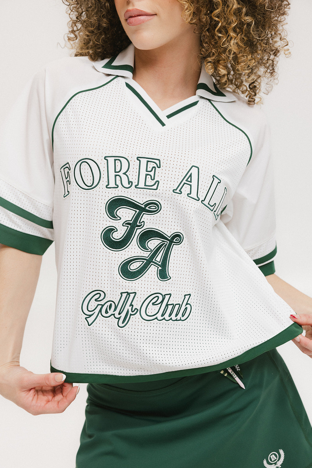 A woman wearing a white rugby-inspired polo shirt with green details and text that reads 'FORE ALL Golf Club'.