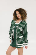 A woman modeling a pinstripe green and white cardigan with intarsia knit details, applique logos, and a button-up closure.