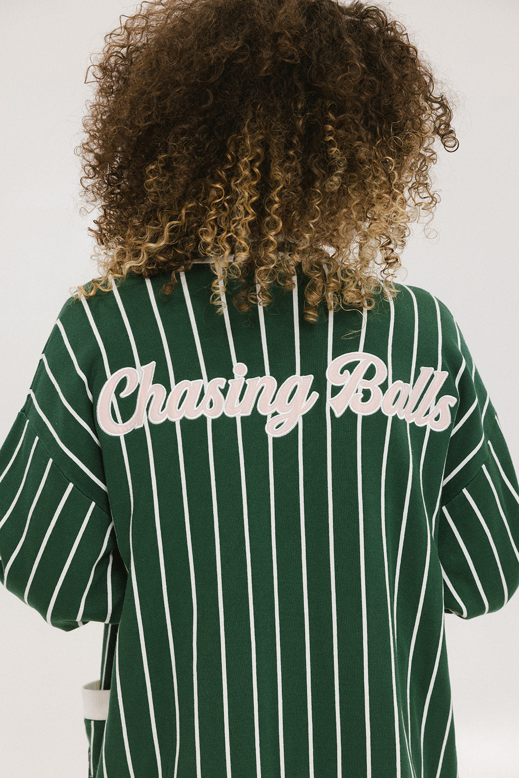 Person wearing a green and white striped cardigan with 'Chasing Balls' text.