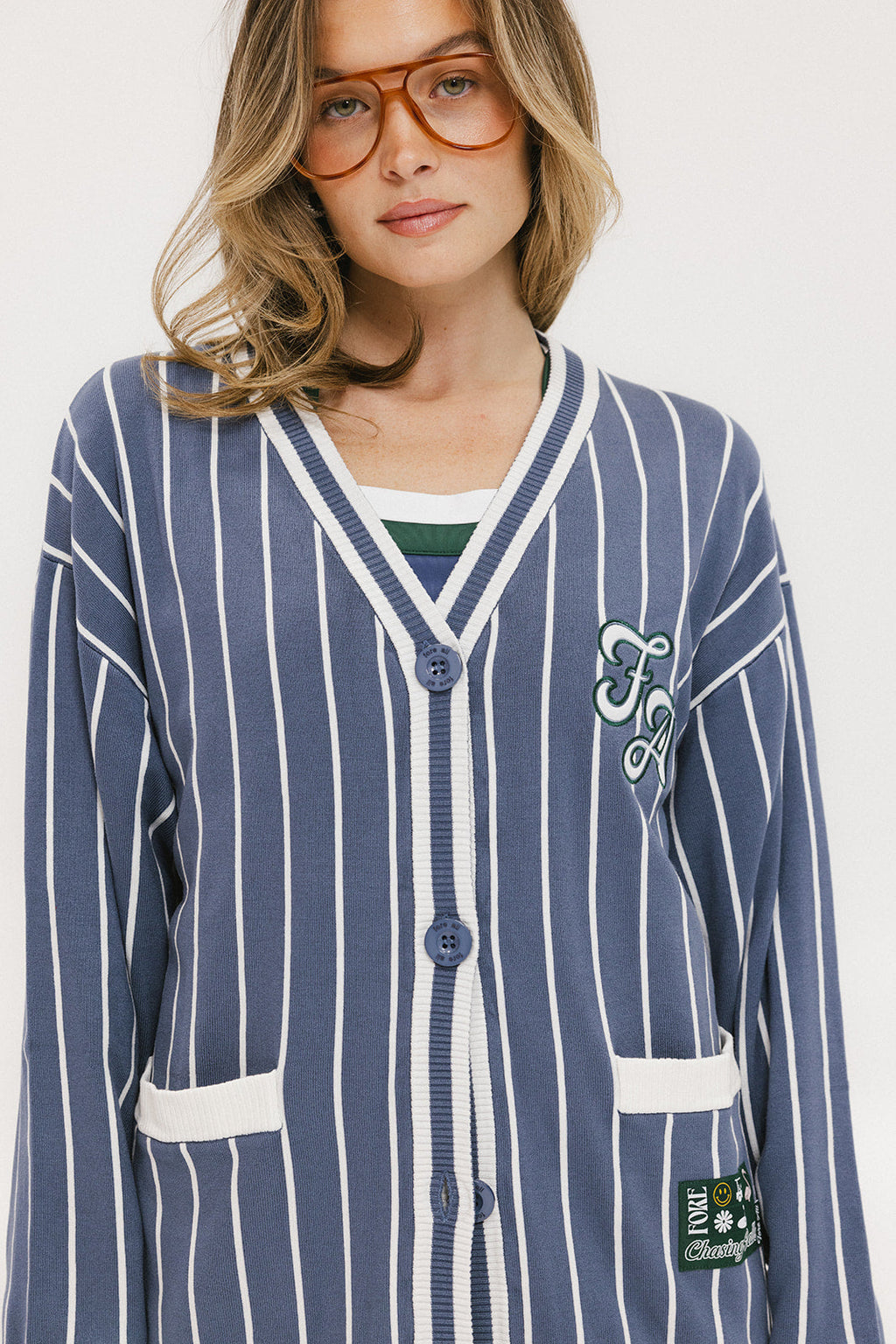 A woman wearing an oversized blue and white pinstripe cardigan with intarsia knit details and applique logos, paired with an indigo dress.