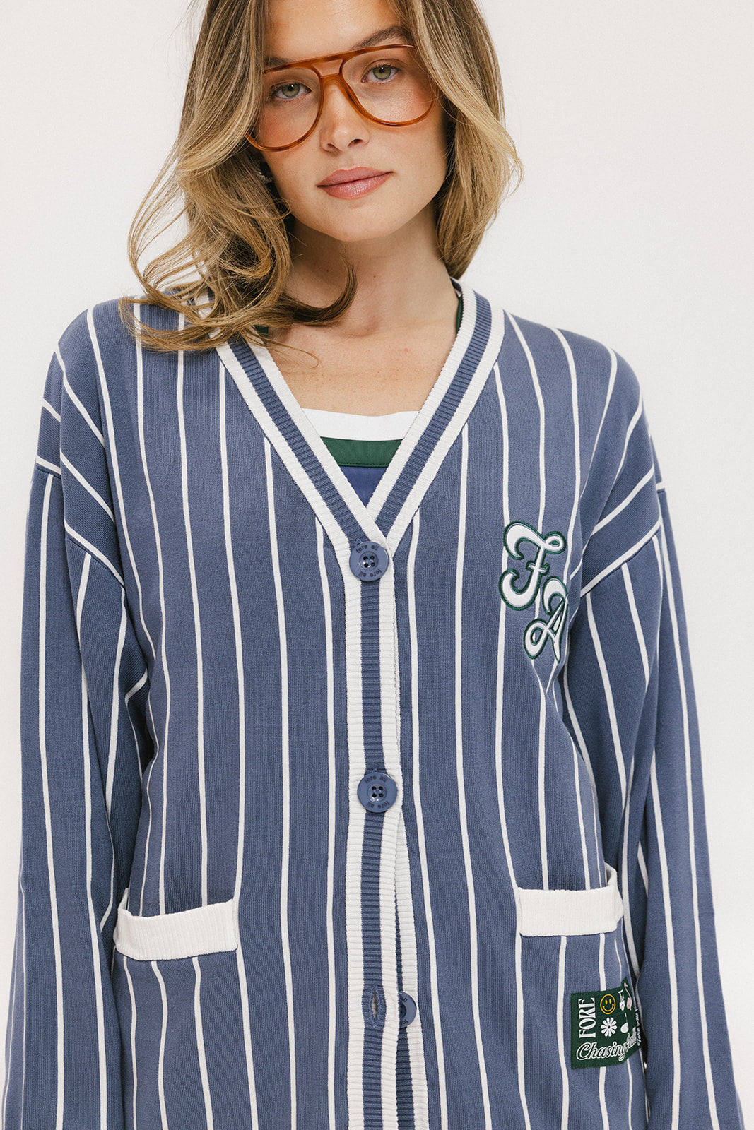 A woman wearing an oversized blue and white pinstripe cardigan with intarsia knit details and applique logos, paired with an indigo dress.